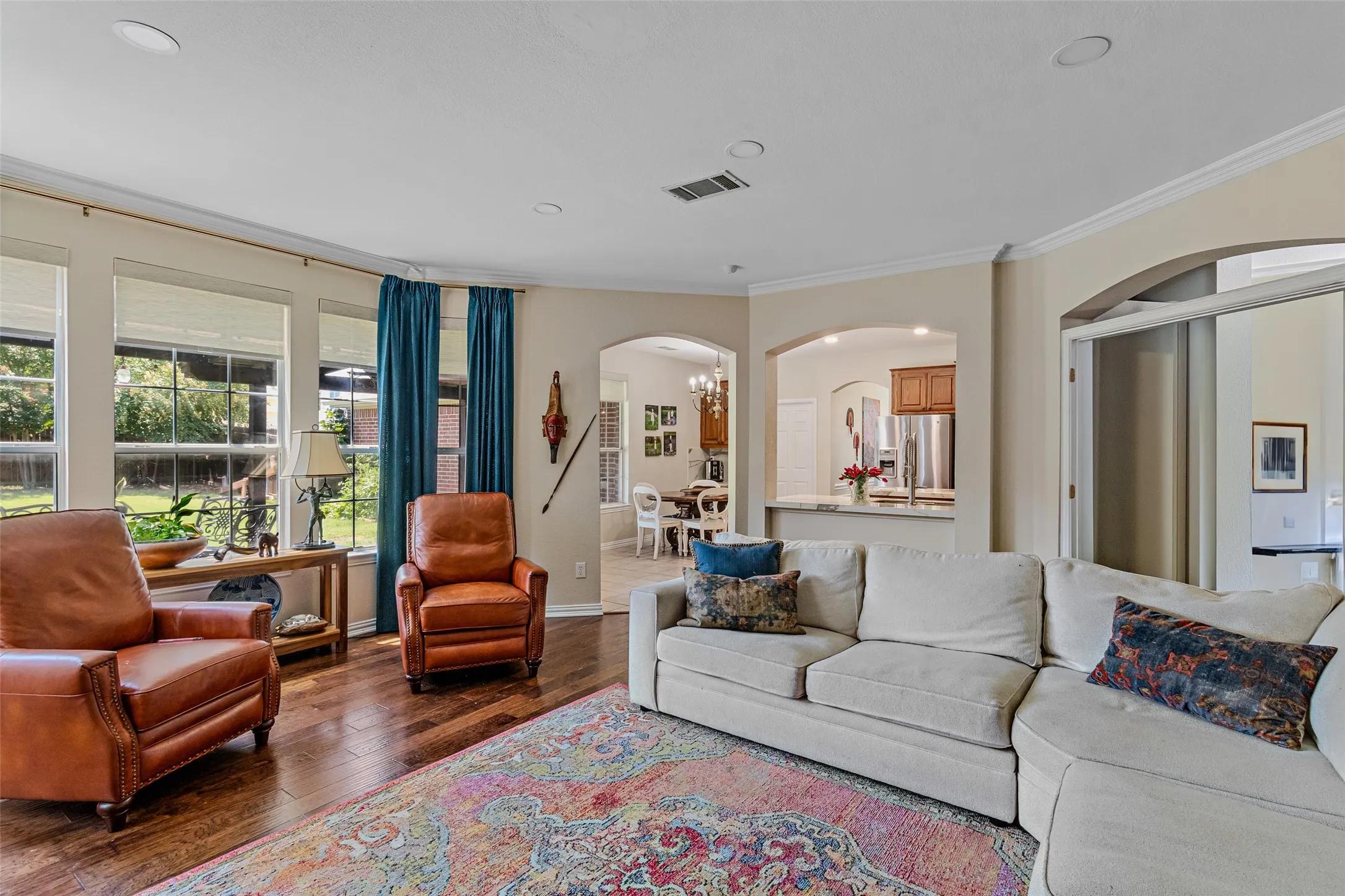 Spacious living area featuring wood-finish flooring, numerous windows with blinds, architectural archways, and recessed lighting