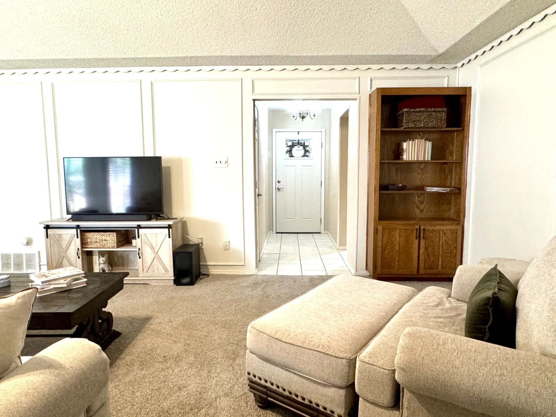 Entry OPENS to Living Room featuring light-toned carpet, white paneled walls, and a recessed entryway with tile flooring