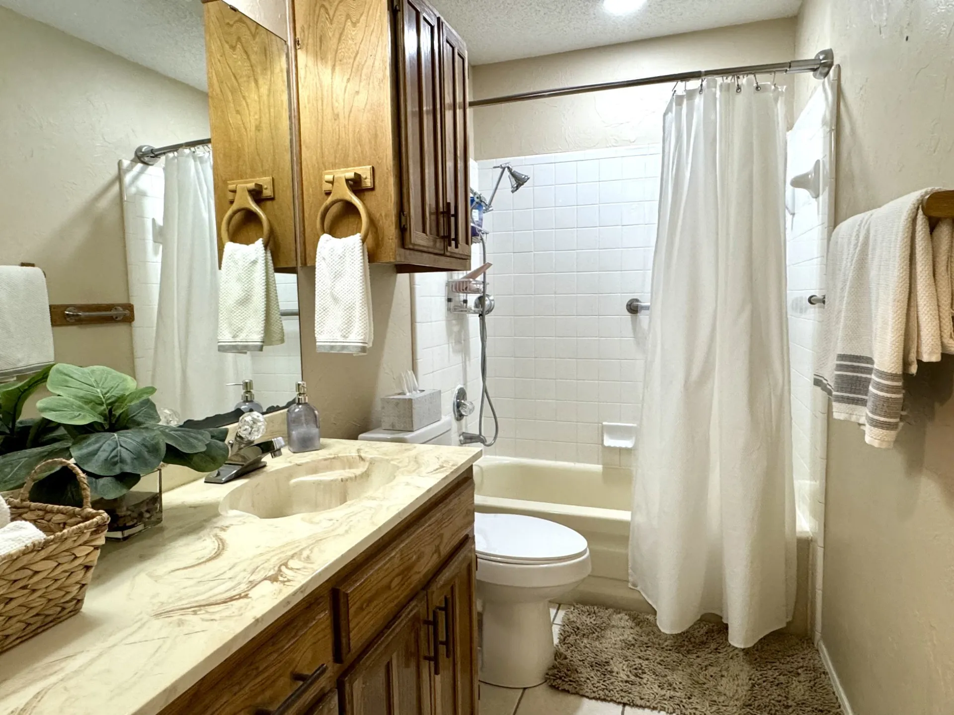 FULL Hall Bathroom has a Tub/Shower Combo: featuring a single-sink vanity with a marble-like countertop, wood-finish cabinetry, a mirror, and overhead wood-finish storage