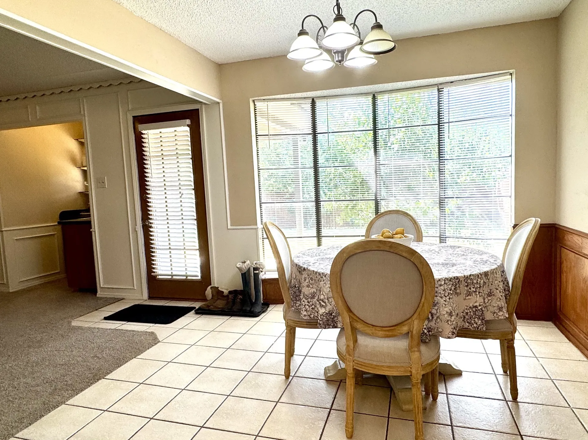 Dining area featuring large bay windows, ceramic tile flooring, a multi-light chandelier, and wainscoting with wood paneling