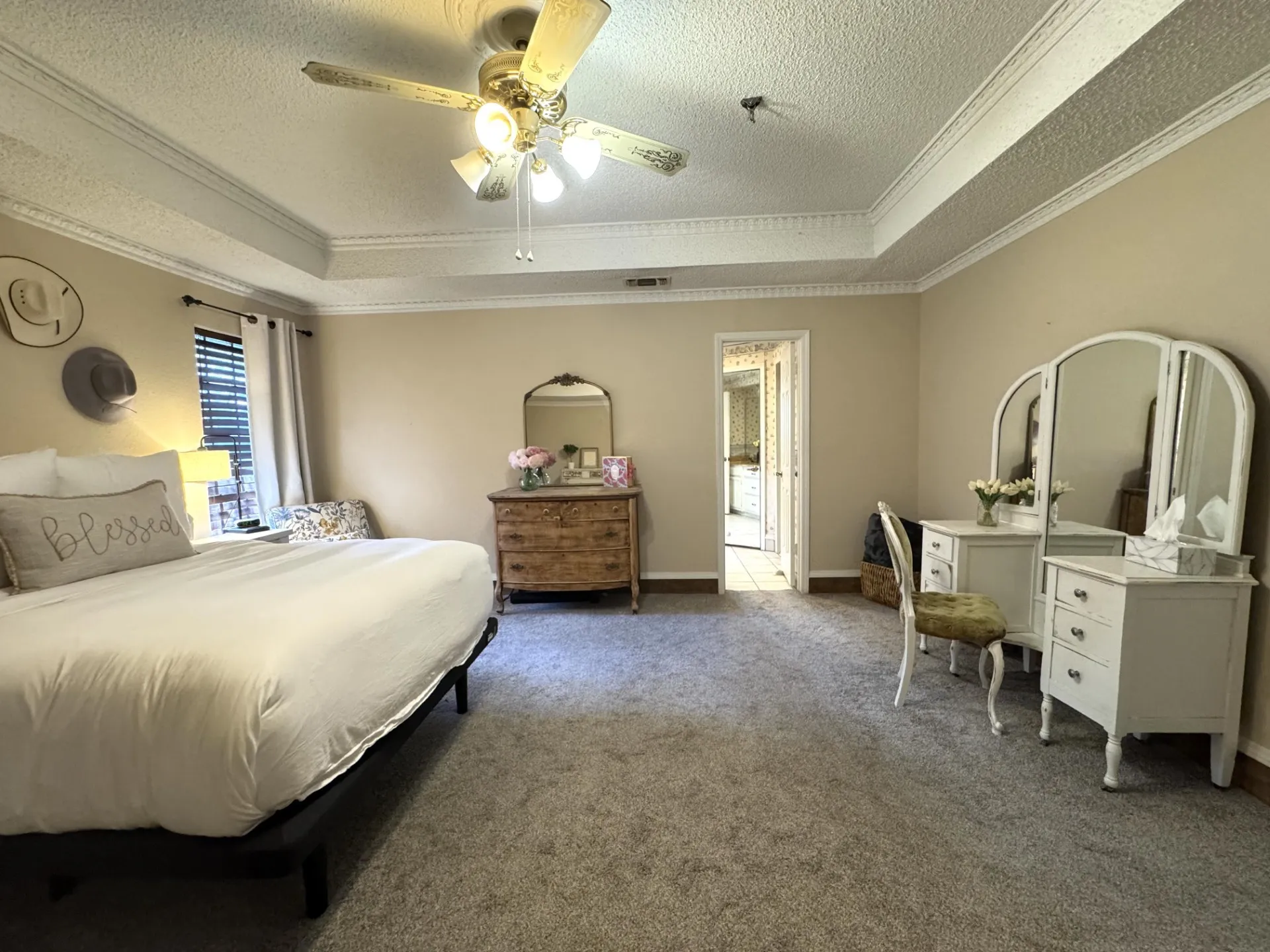 Spacious Primary Bedroom features Ensuite Bath, tray ceilings with detailed crown molding, a ceiling fan with integrated lighting, and neutral tone carpeting