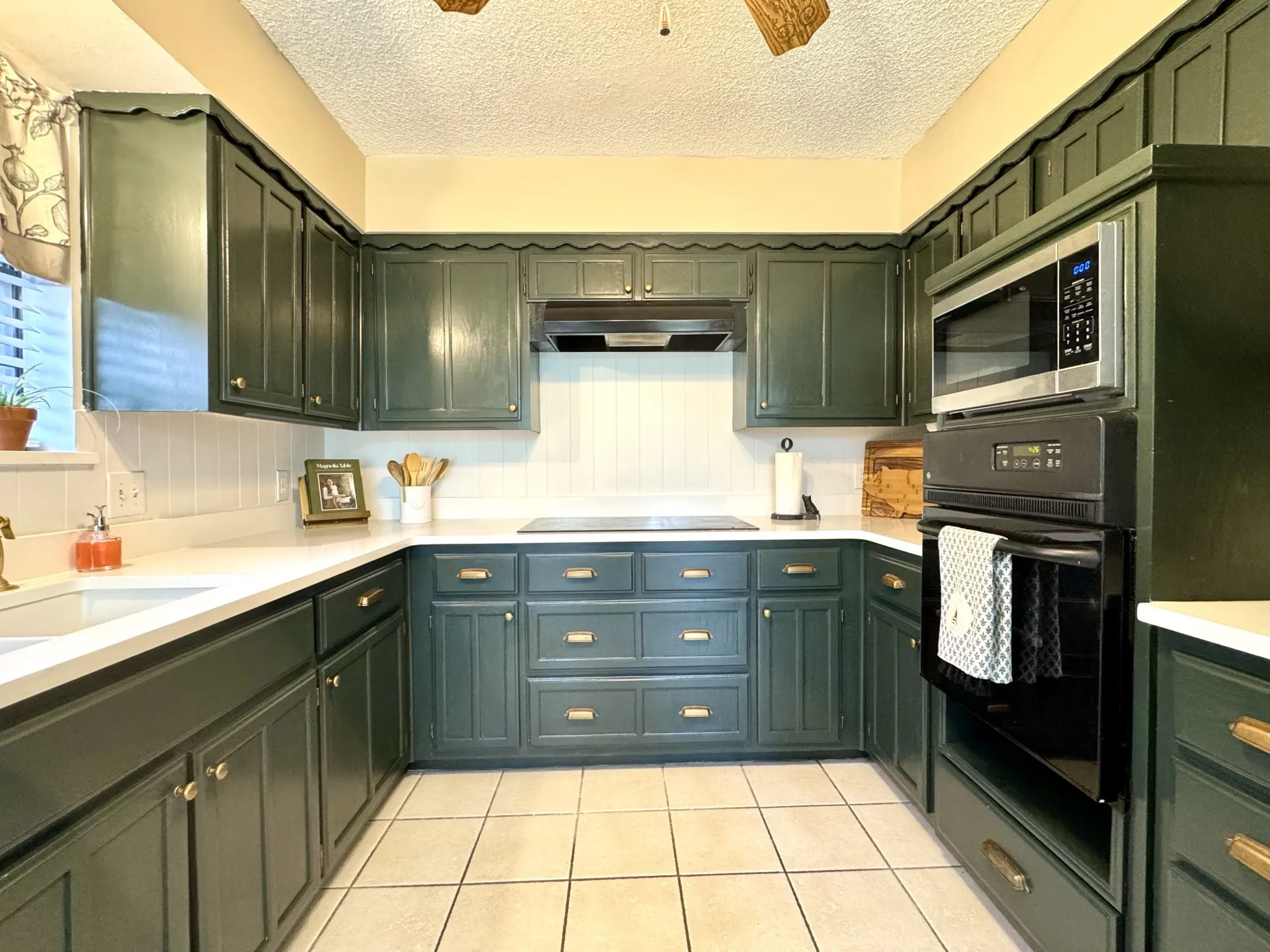 MAGNOLIA Inspired dark green kitchen cabinetry, white QUARTZ countertops, smooth glass electric COOKTOP, beadboard backsplash, tile flooring, and integrated appliances.