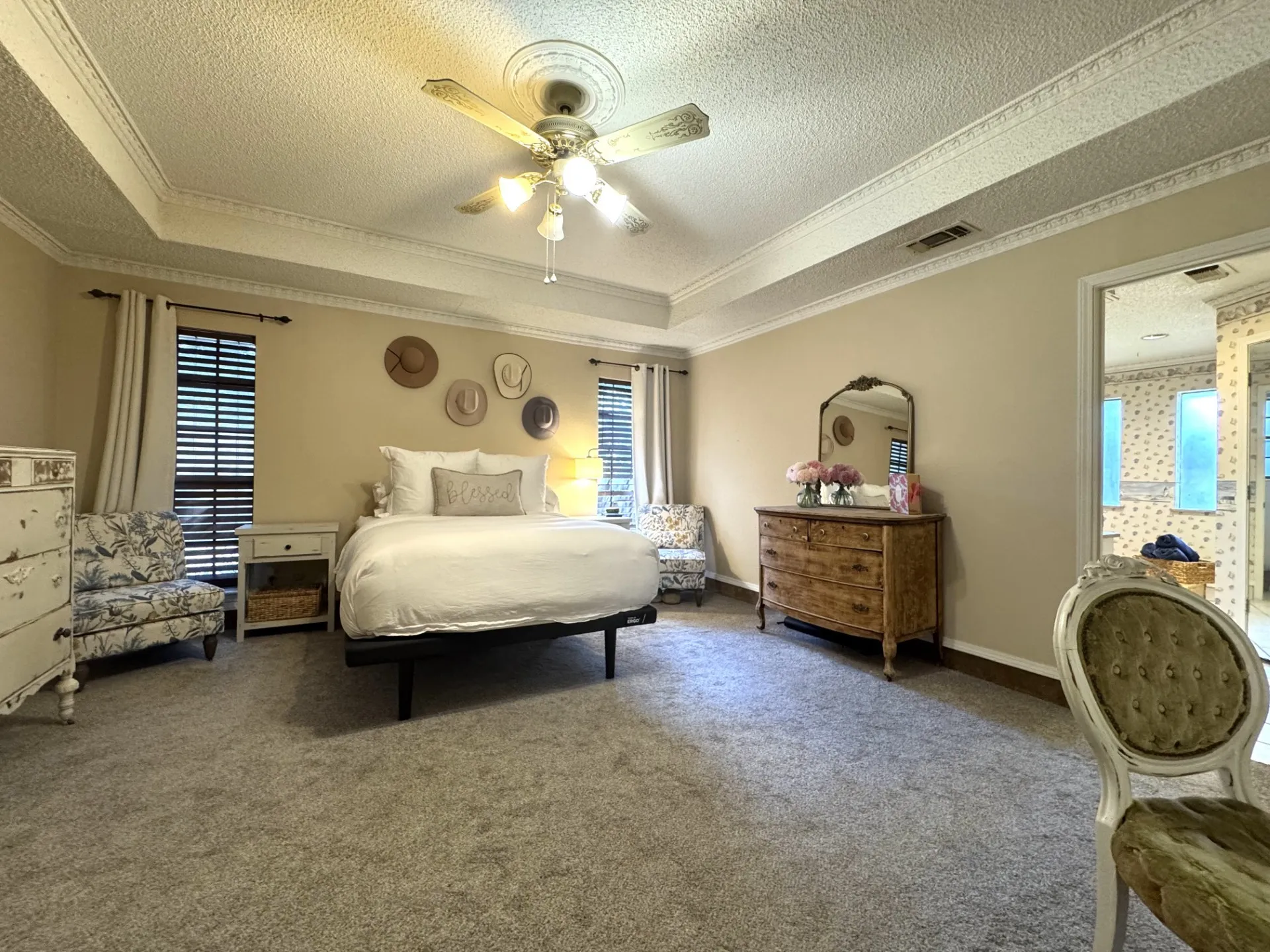 Spacious Primary Bedroom featuring tray ceilings with decorative molding, ceiling fan, and carpet flooring