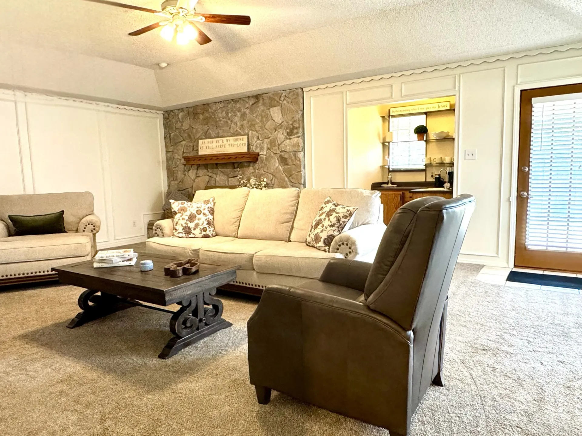 Spacious living area featuring a vaulted ceiling with a ceiling fan, stone fireplace, wet bar, and wainscoting detailing.