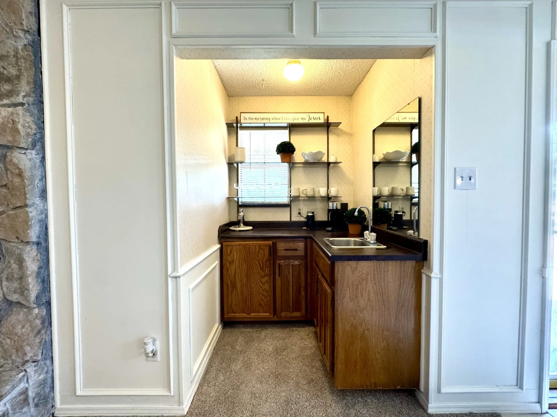 Built-in WET BAR in Living Room featuring a stainless steel sink, dark countertops, wood cabinetry, and wall-mounted shelving