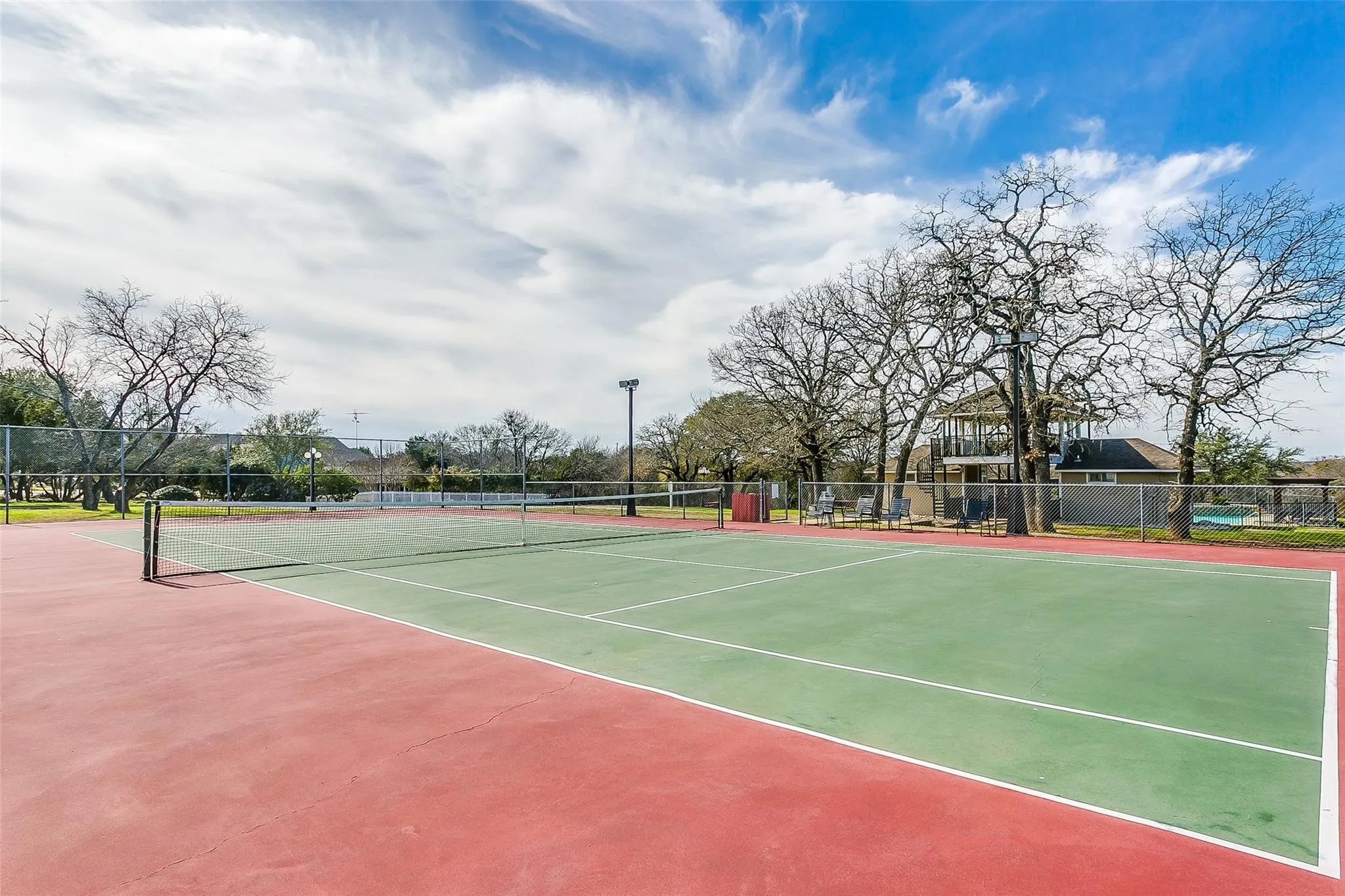 Tennis court featuring a red and green playing surface, perimeter fencing, and mature trees