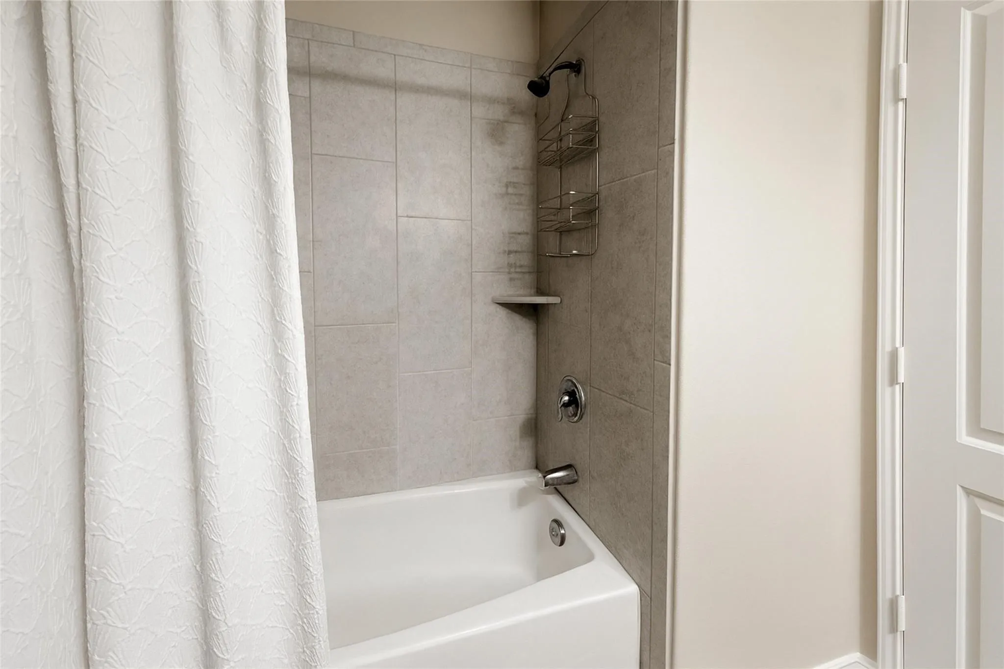 White bathtub with chrome fixtures and light-toned wall tiling