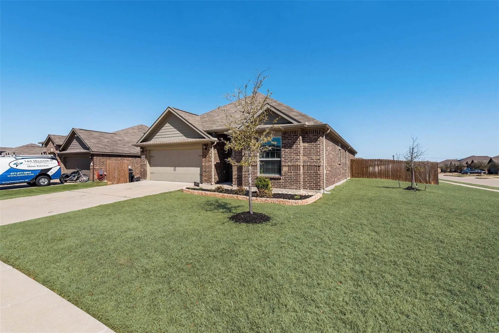 Brick exterior with a gabled roofline, an attached garage, a concrete driveway, and a front yard with a landscaping bed