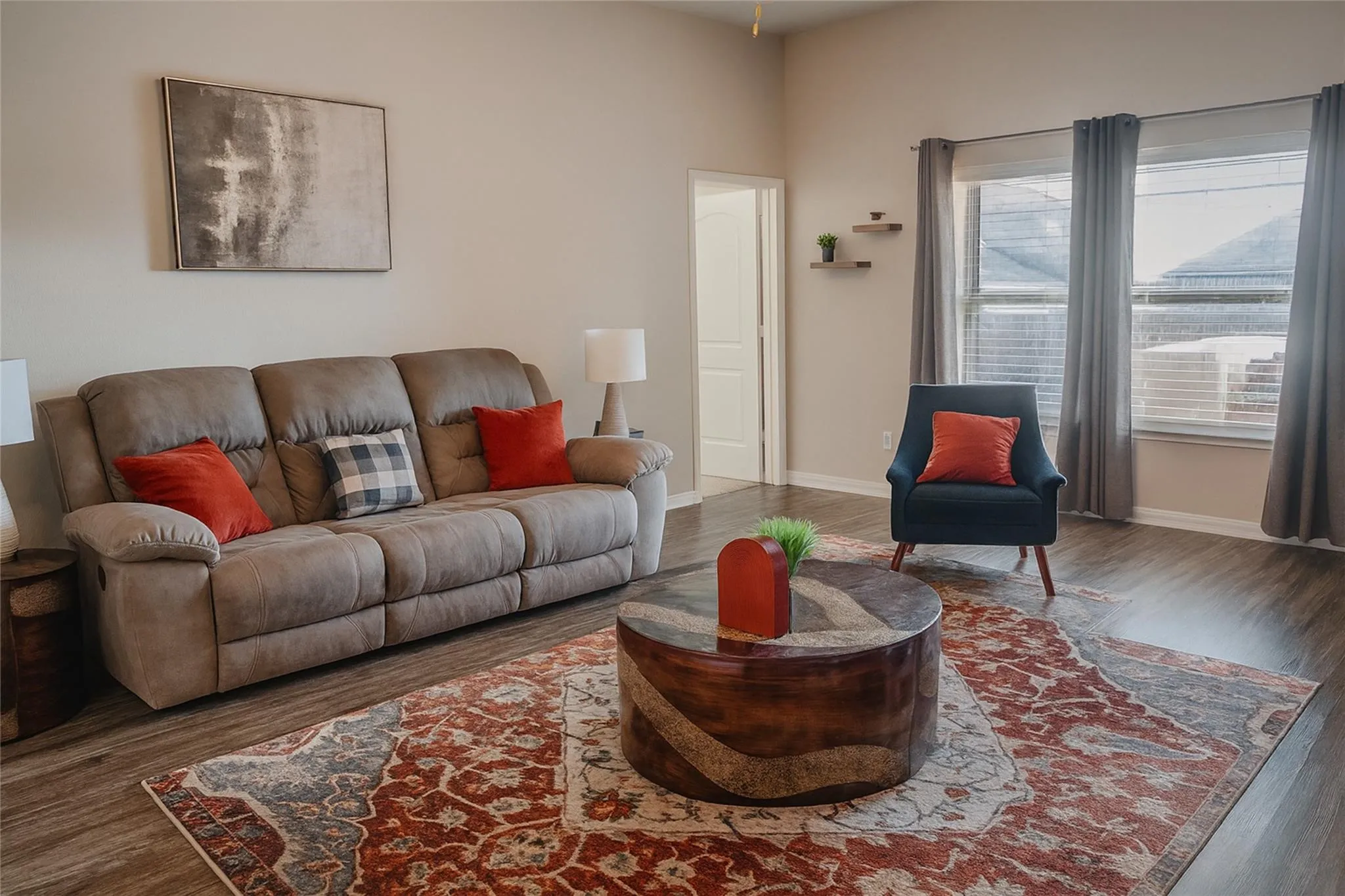Spacious living area featuring wood-finish flooring, light-toned walls, and multiple windows with blinds
