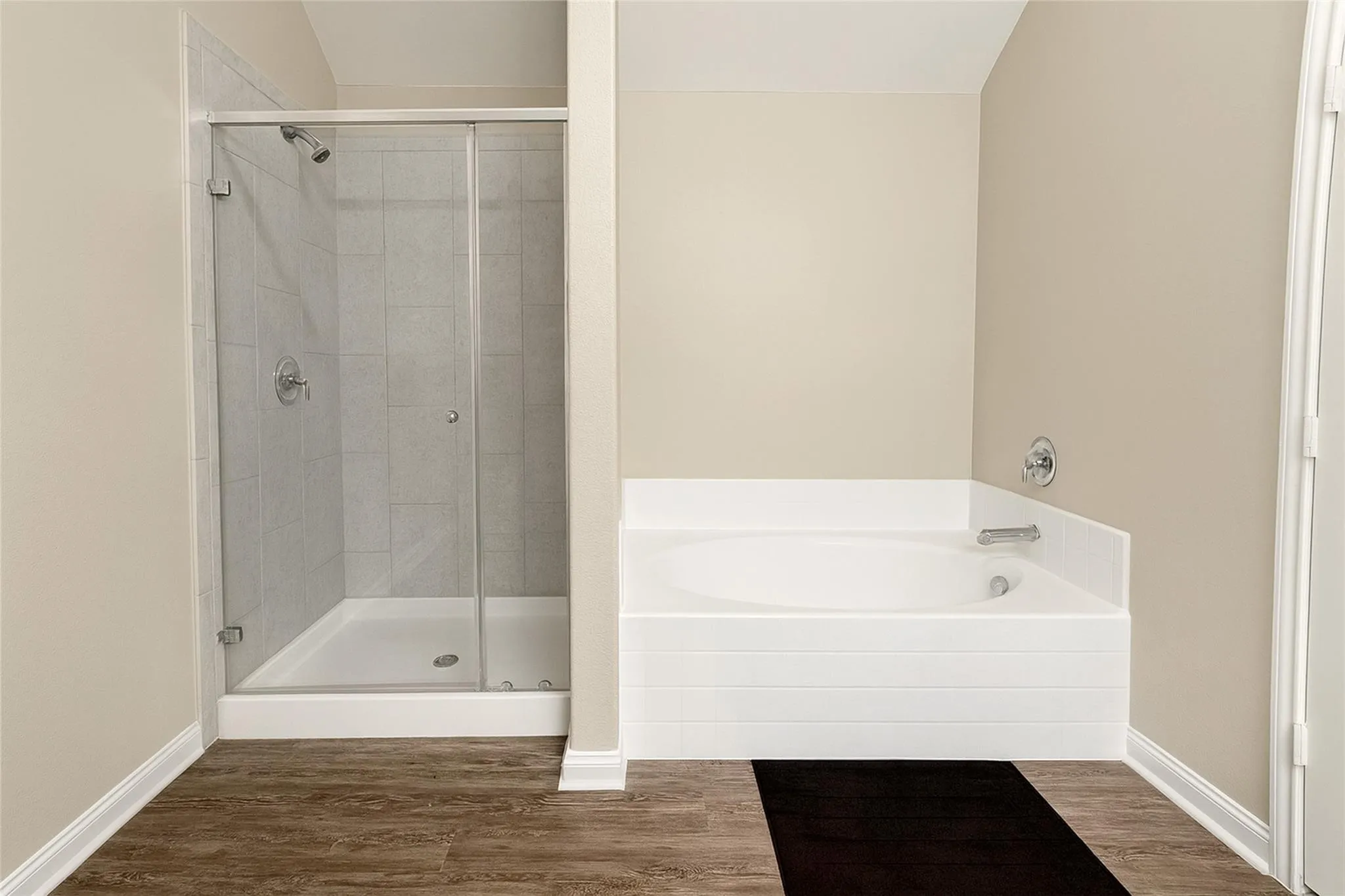 Bathroom featuring a glass-enclosed shower with tile surround, a built-in soaking tub, wood-finish flooring, and light neutral wall paint
