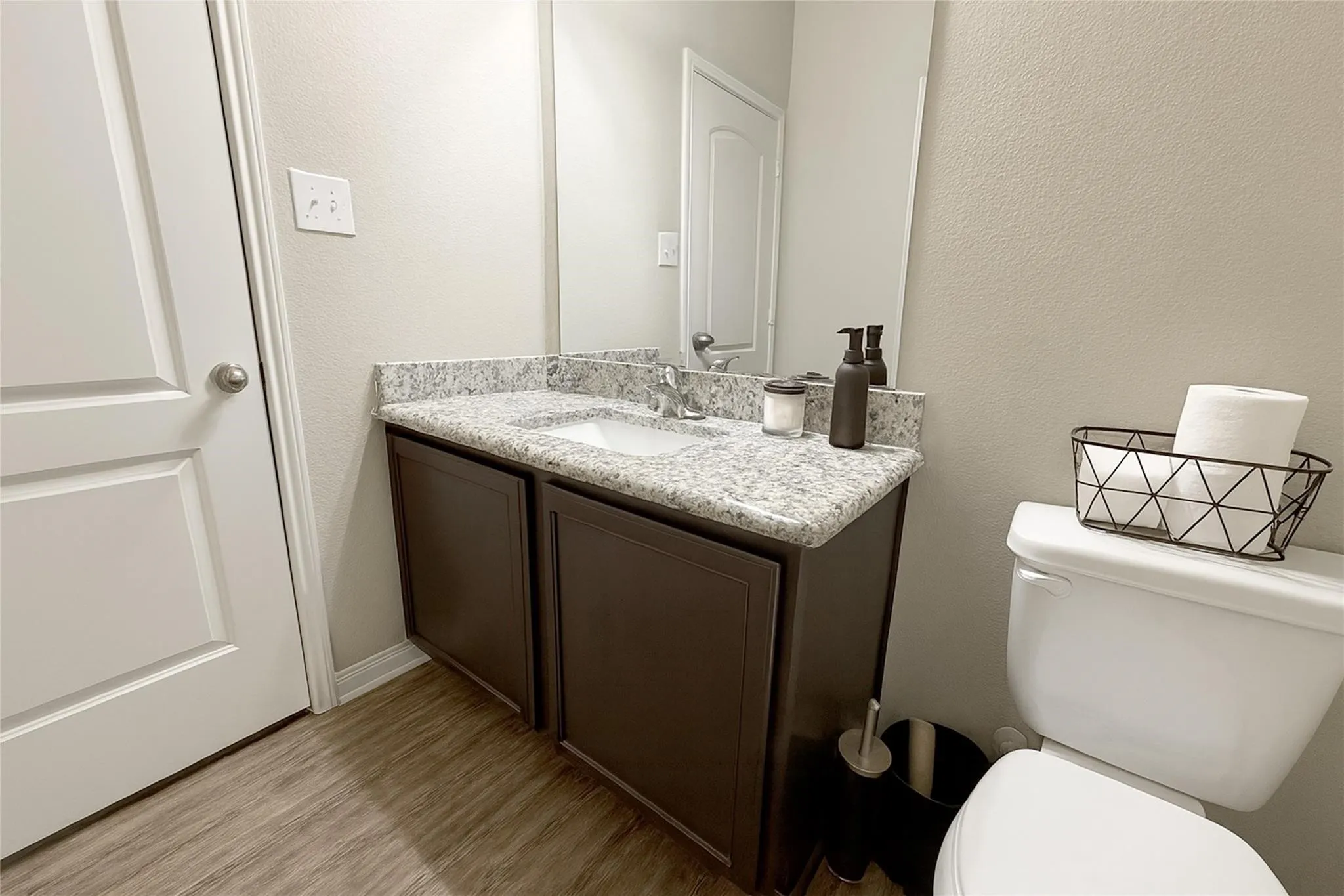 Bathroom vanity featuring a granite-style countertop, undermount sink, dark wood-finish cabinetry, and wood-finish flooring