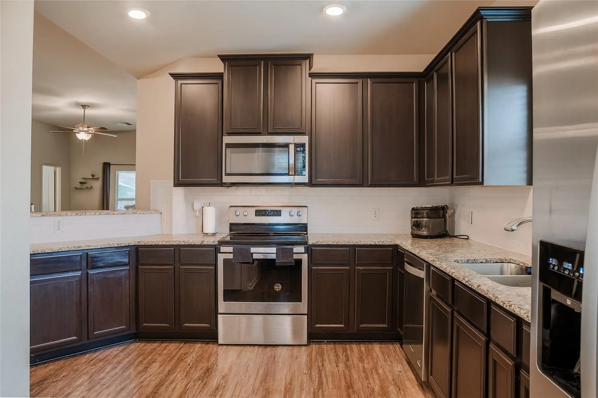 Kitchen featuring dark wood cabinetry, light-toned countertops, a white subway tile backsplash, stainless steel appliances, and wood-finish flooring