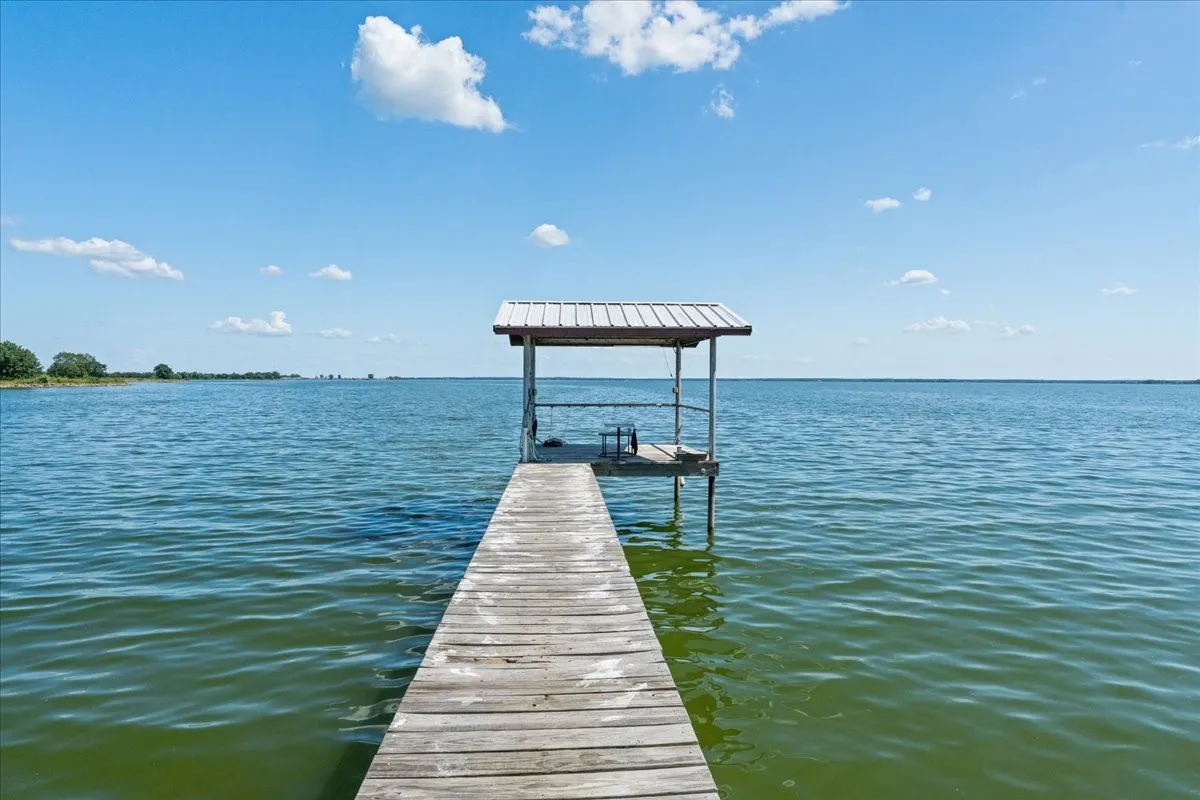Private wooden dock extending into open water, featuring a covered boat slip with a metal roof