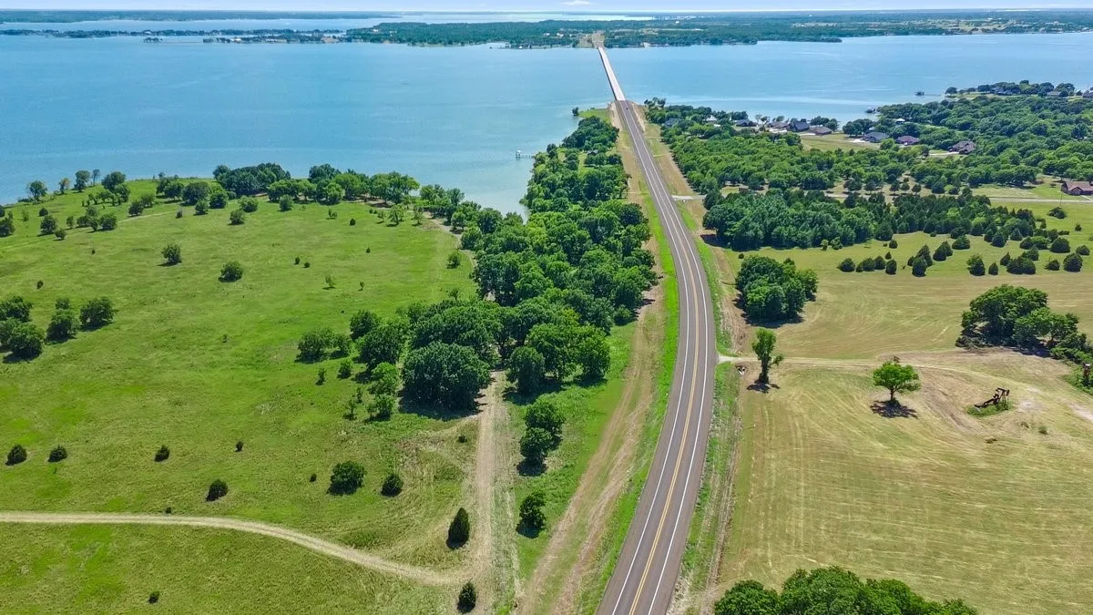Expansive waterfront landscape featuring a significant body of water, a prominent bridge, and a paved road