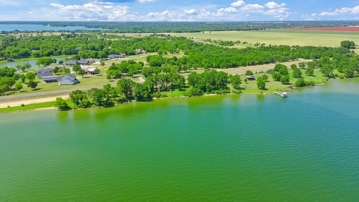 Expansive waterfront property featuring a private dock, lush green landscaping, mature trees, and a substantial land area