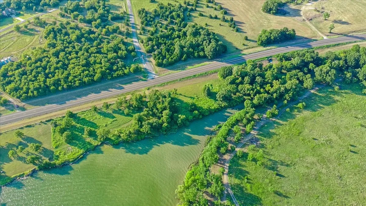Expansive land parcel featuring waterfront access, mature trees, open green spaces, and highway frontage