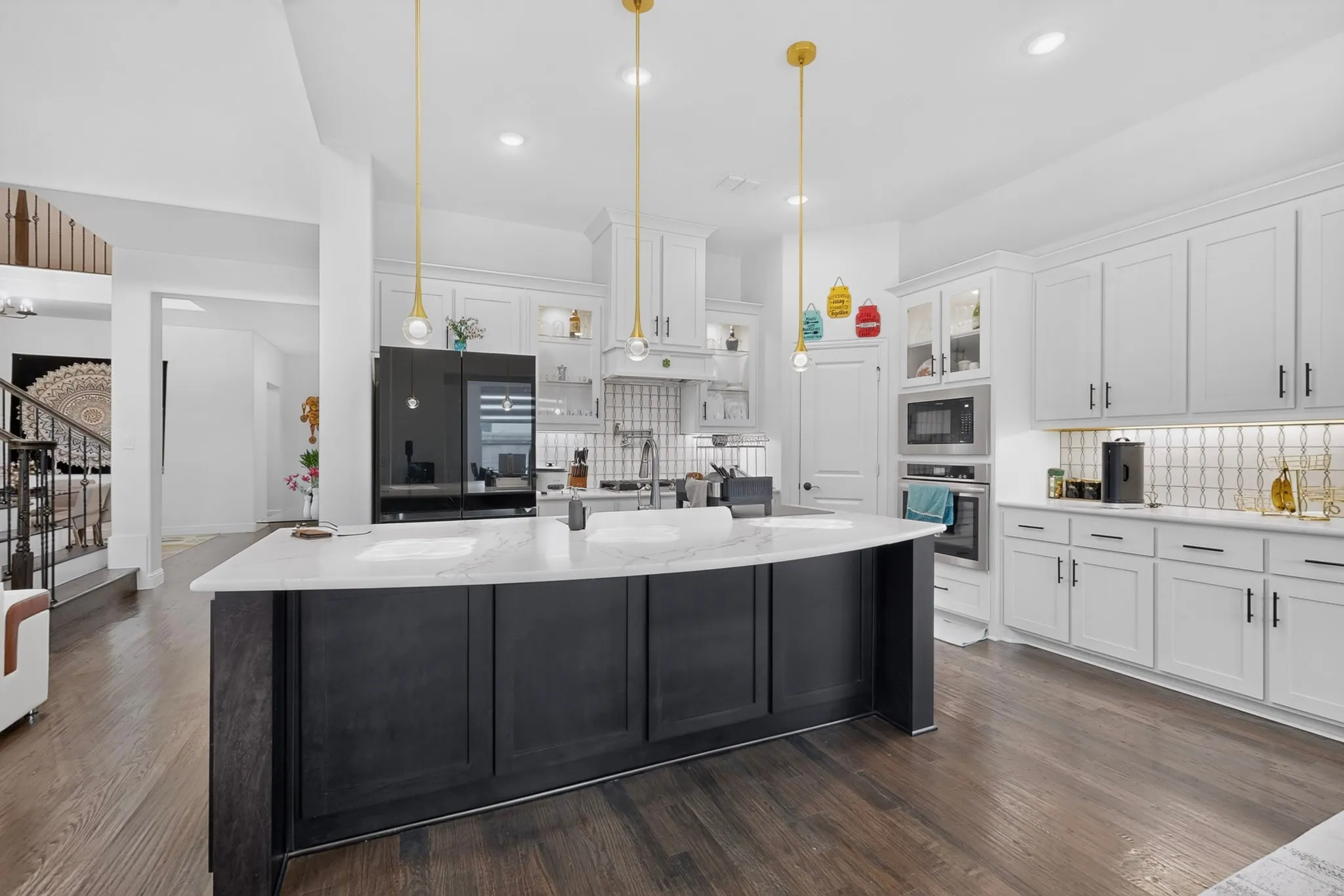 Spacious kitchen featuring a large dark-toned island with a white countertop, white cabinetry, dark wood-finish flooring, and gold-finish pendant lighting