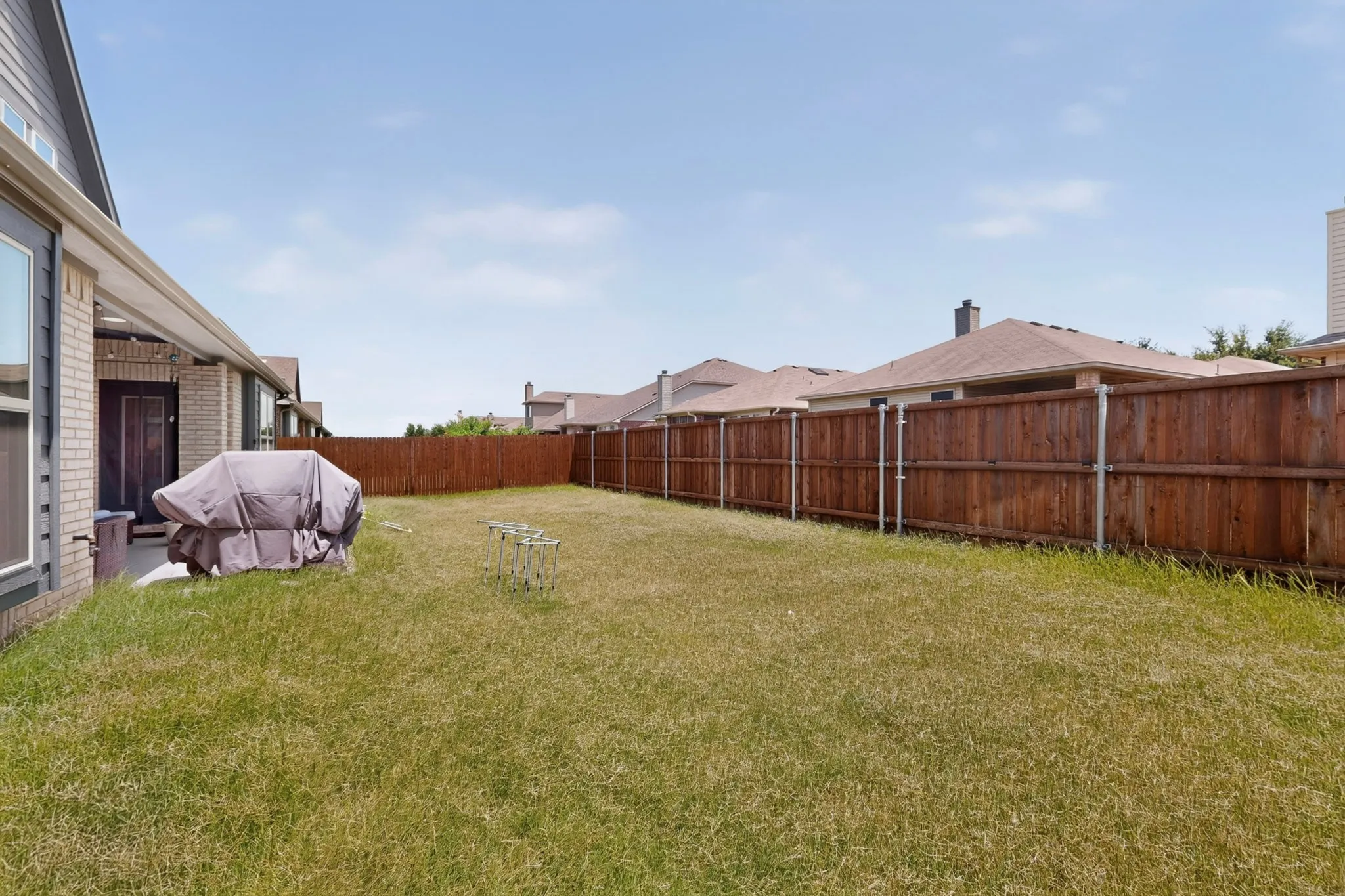 Expansive backyard featuring a privacy fence, a covered patio, and a brick exterior with large windows