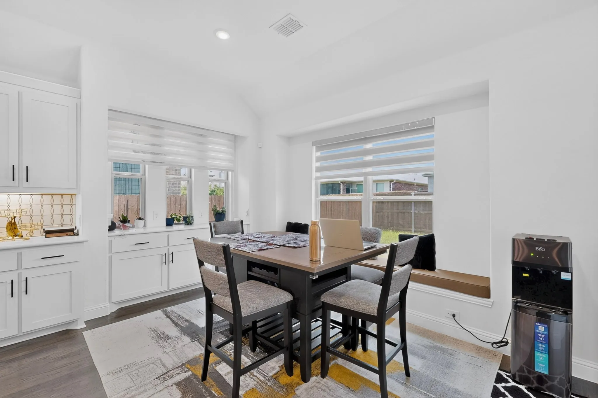 Kitchen dining area featuring a built-in window bench, white shaker cabinetry, patterned tile backsplash, and wood-finish flooring