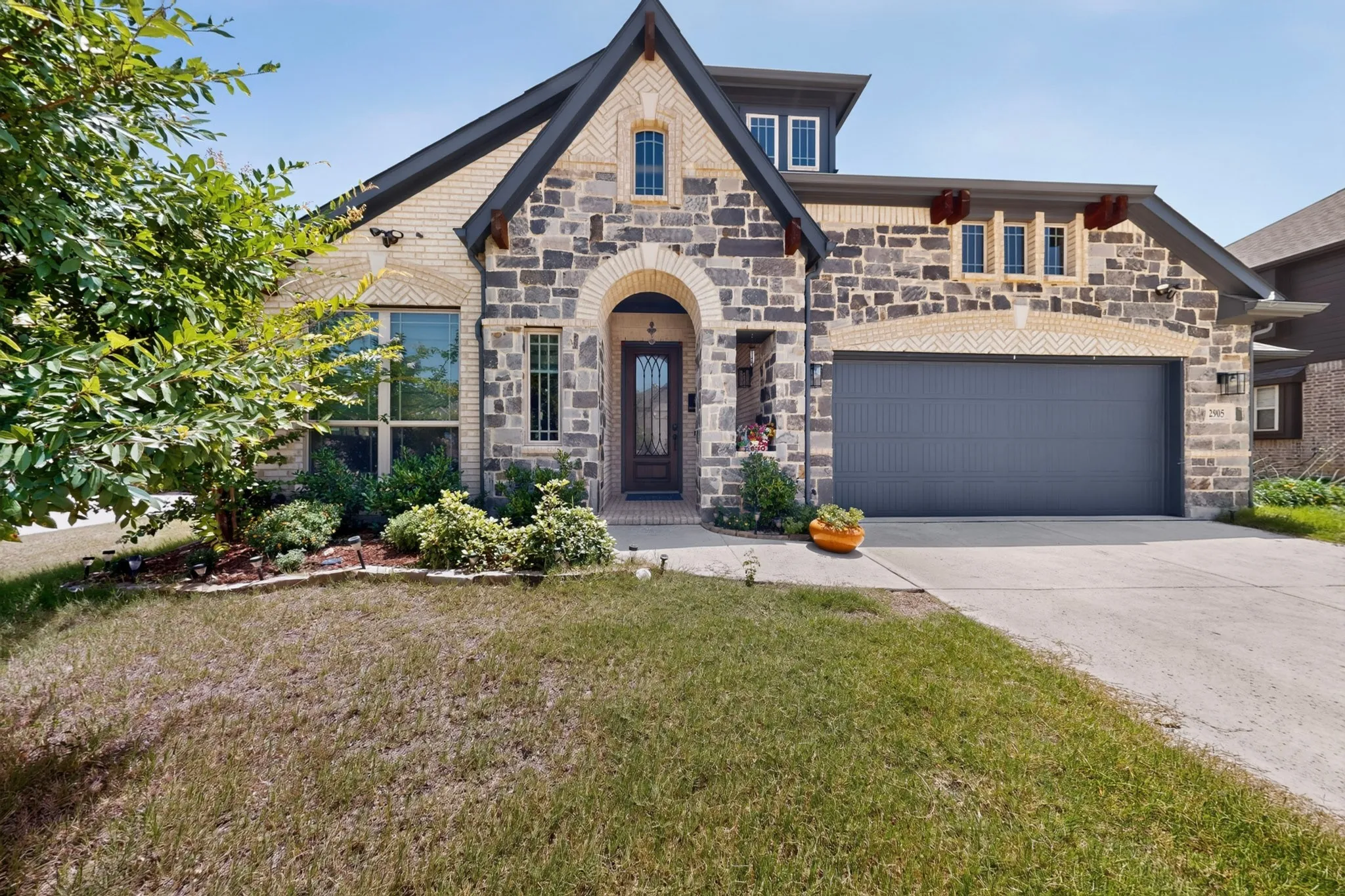 Stone and brick facade featuring a dark gray garage door, arched entry, and a dormer window