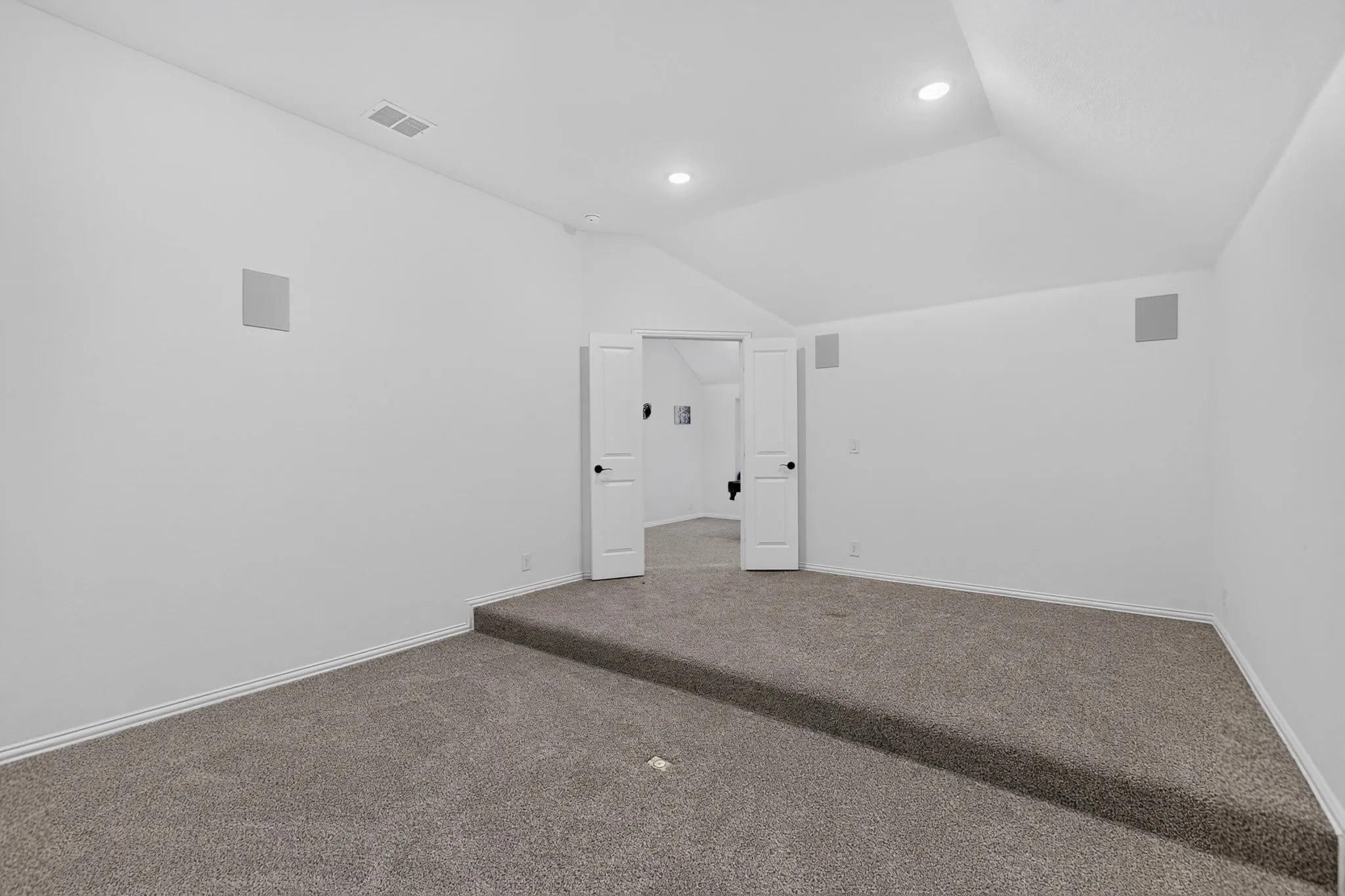 Carpeted room featuring a raised floor section, vaulted ceiling, recessed lighting, and wall-mounted speakers