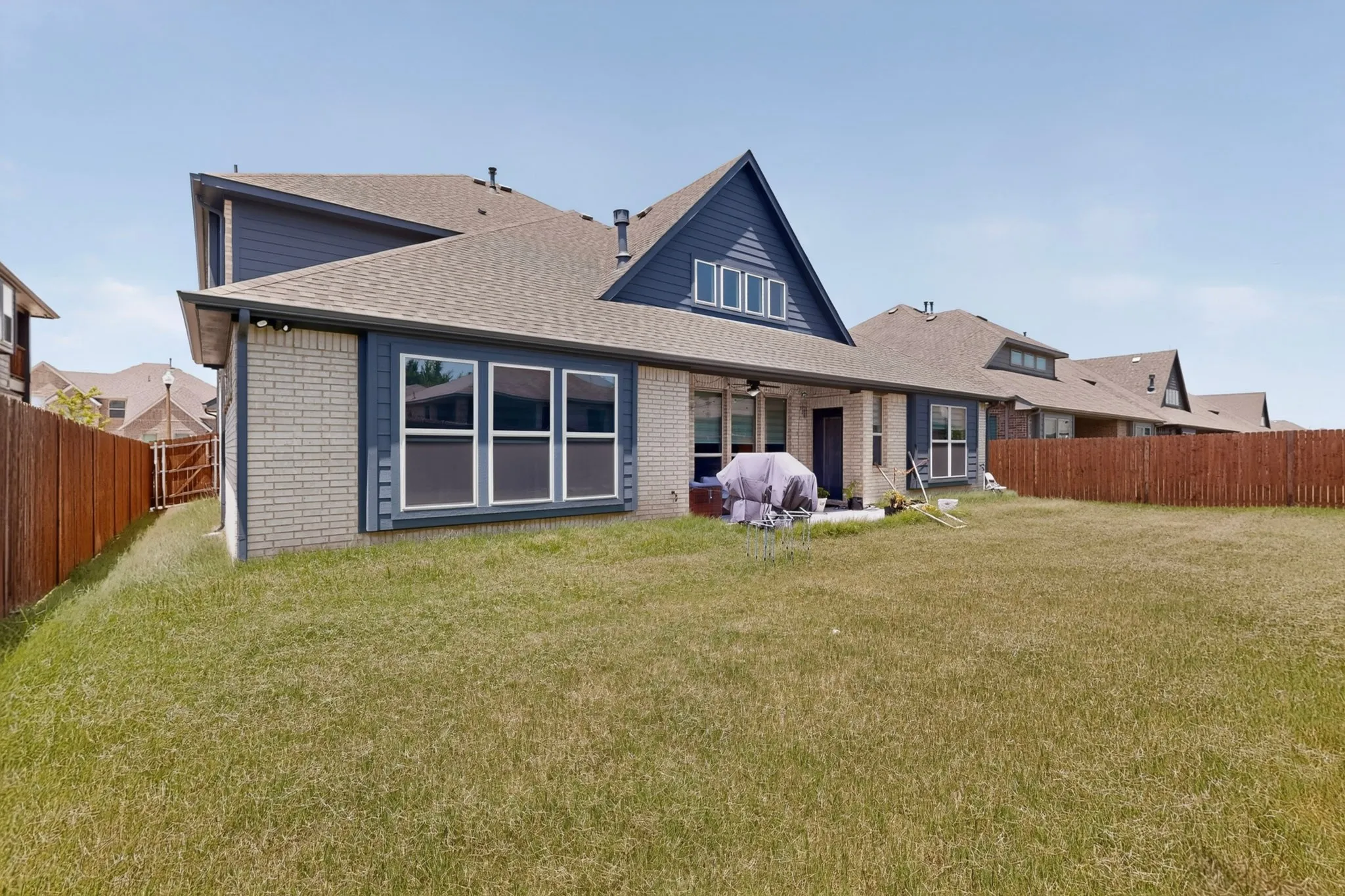 Expansive backyard featuring a light brick exterior and dark blue siding, a covered patio, a privacy fence, and a dormer window