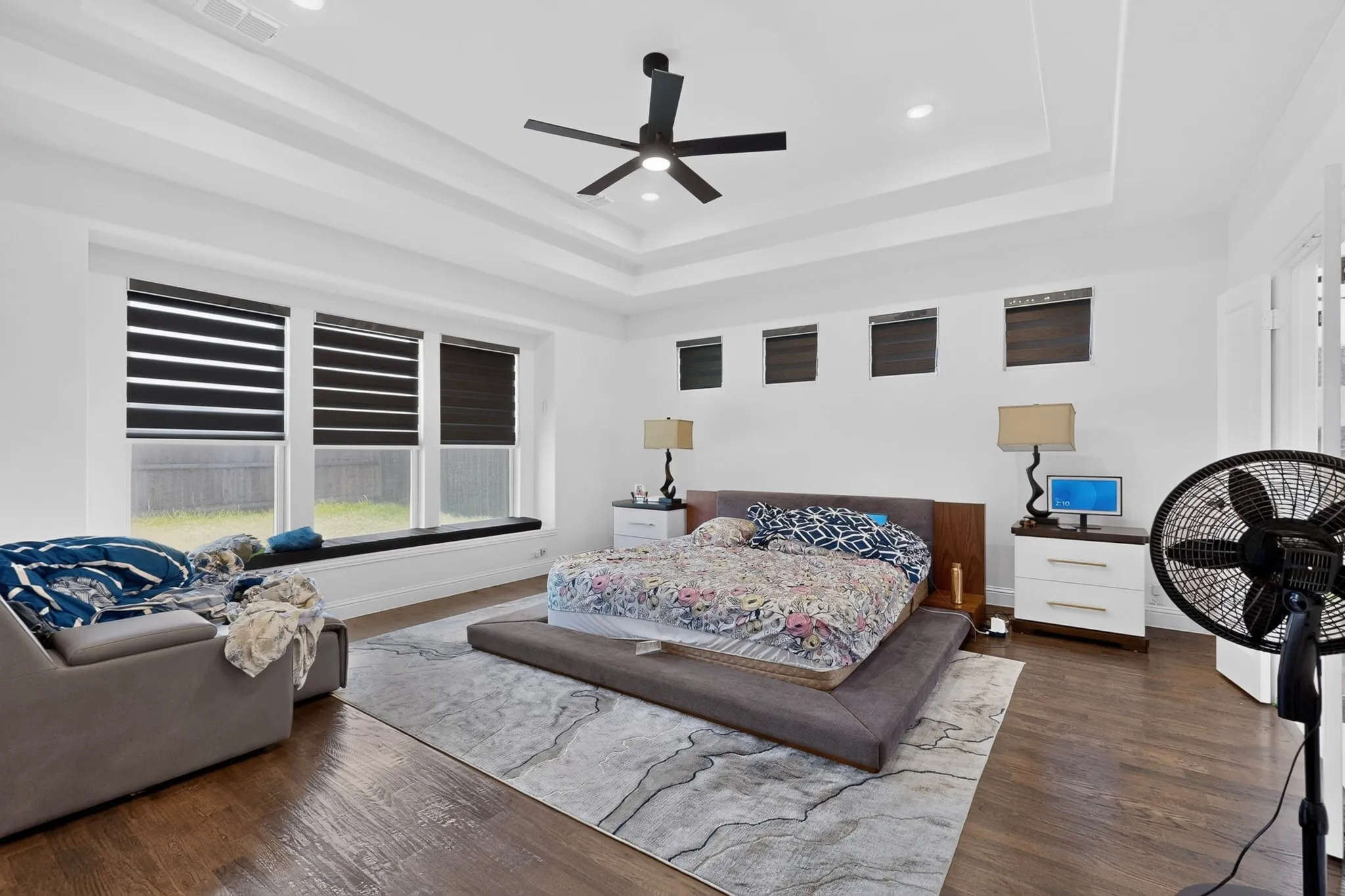 Spacious room featuring rich wood-finish flooring, a tray ceiling with recessed lighting, and a modern ceiling fan