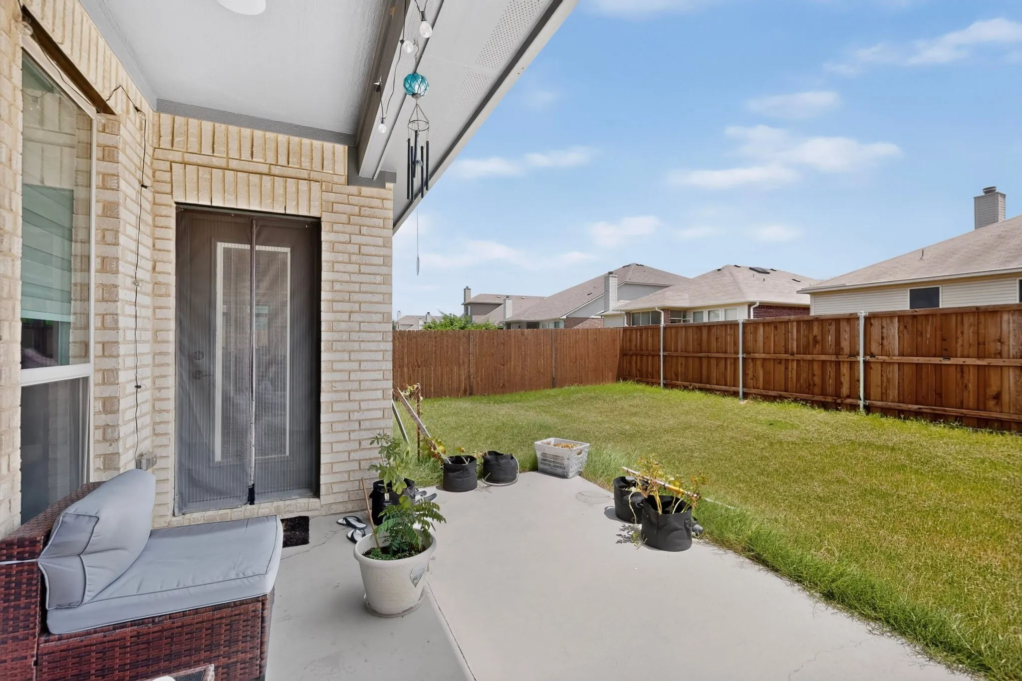 Covered patio with a concrete surface, brick exterior, and a screen door leading to a fenced backyard featuring a grass lawn