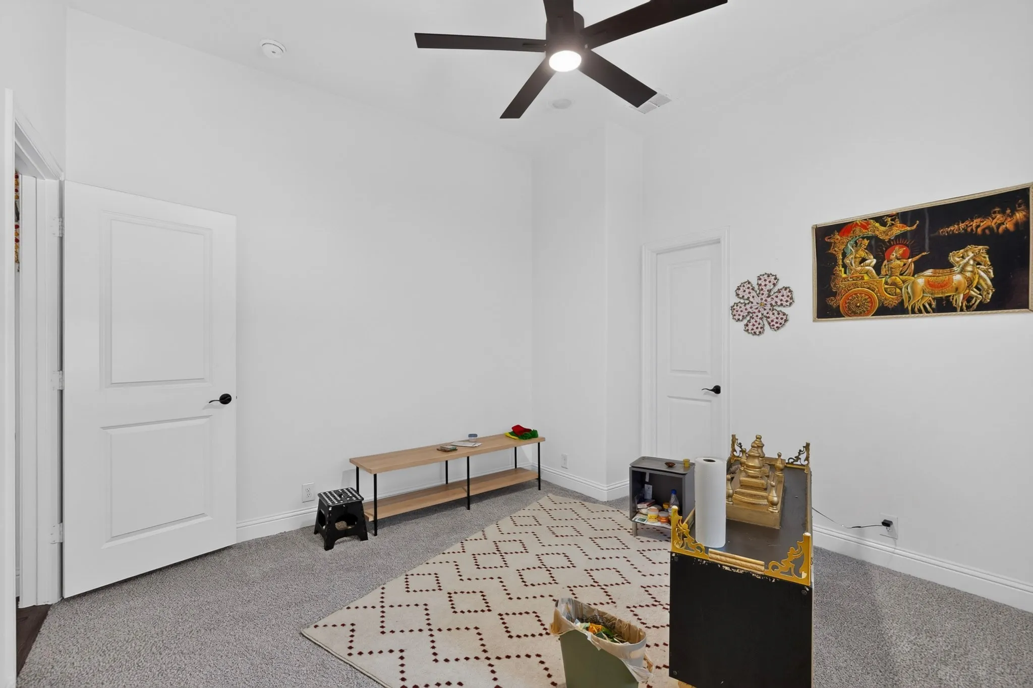 Spacious interior room featuring light gray carpeting, crisp white walls, and a contemporary black ceiling fan with integrated lighting