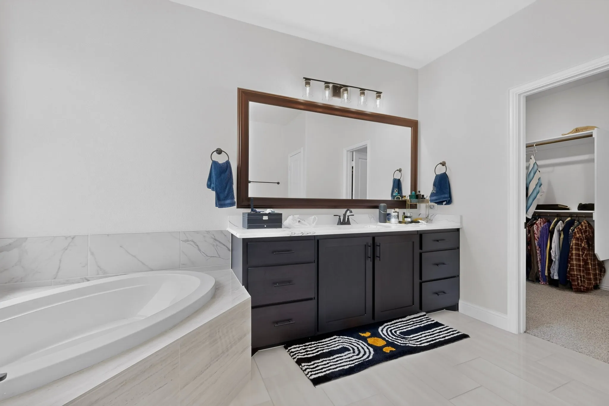 Built-in soaking tub with marble-look tile surround and a dark wood-framed mirror