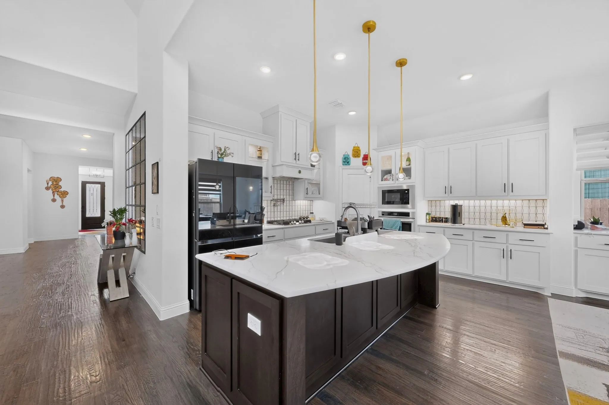 Gourmet kitchen featuring a large central island with a curved countertop, white shaker cabinetry, dark wood-finish flooring, and recessed lighting