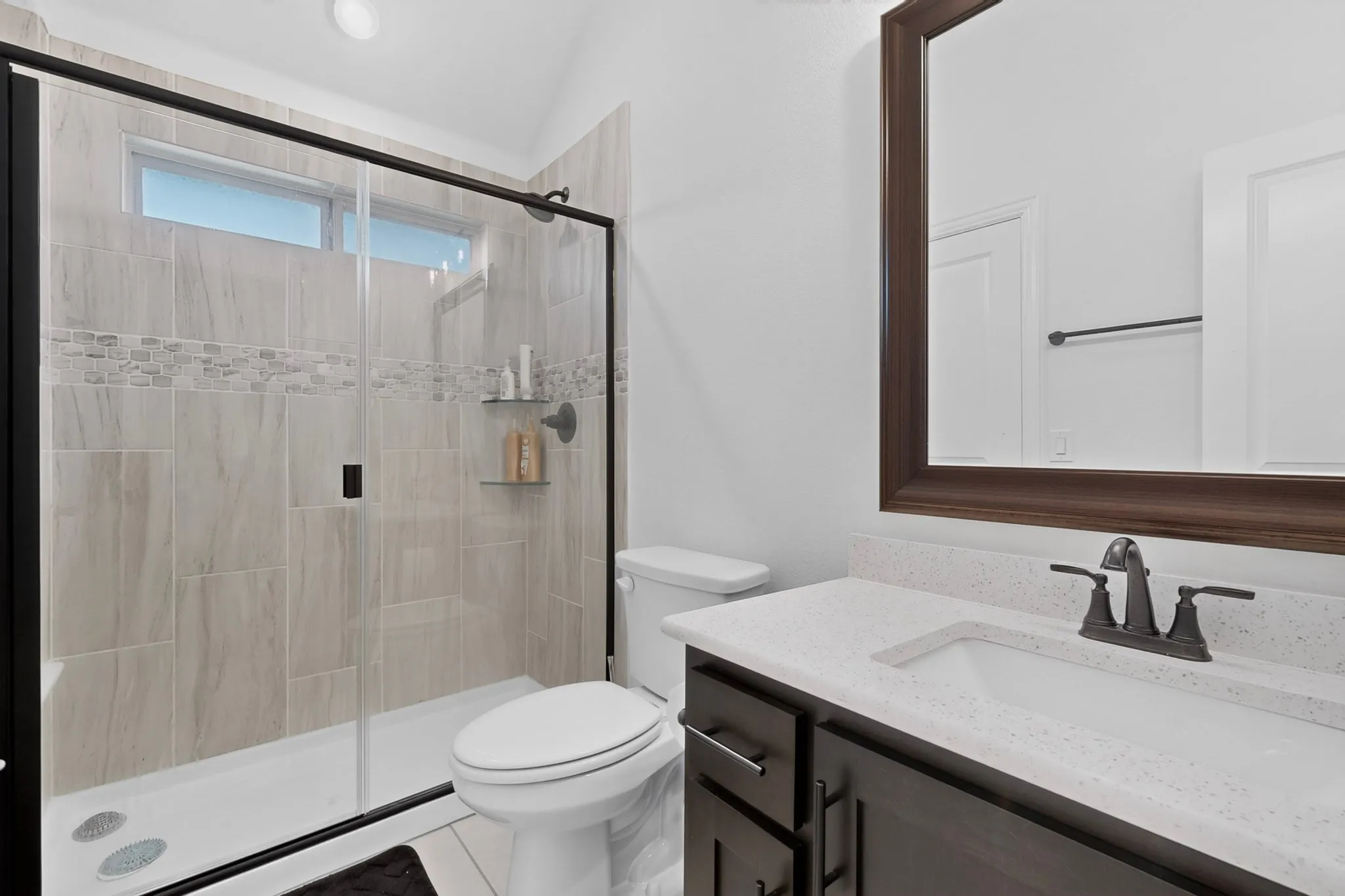 Bathroom featuring a glass-enclosed shower with tile surround, decorative mosaic accent band, and built-in shelving