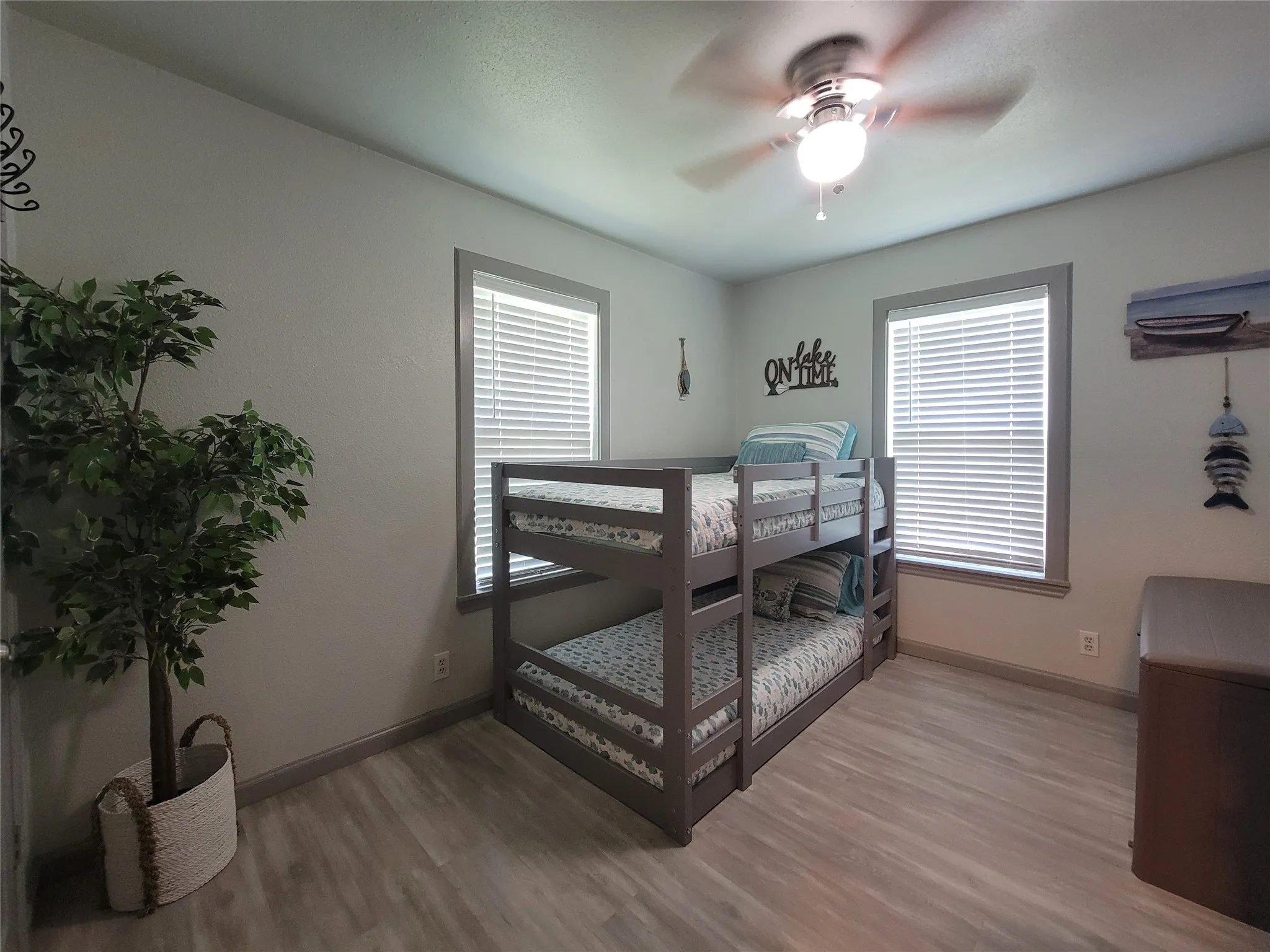 Room featuring wood-finish flooring, two windows with blinds, a ceiling fan with light fixture, and a built-in bunk bed frame