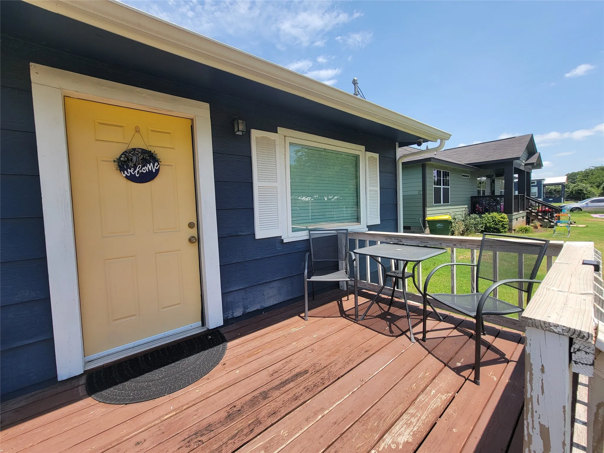 Exterior features a vibrant yellow entry door, white window shutters, and a wooden porch