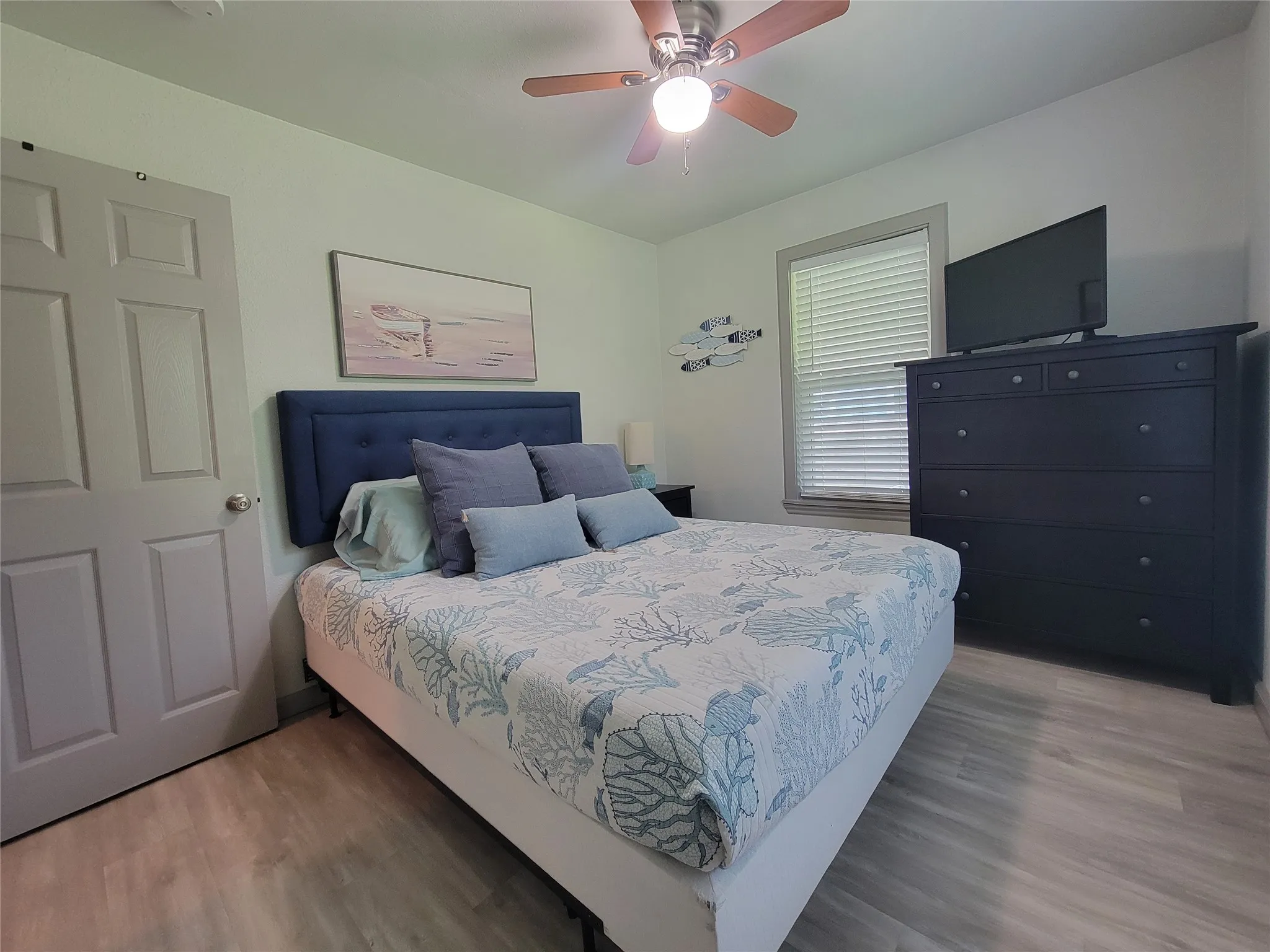 Bedroom featuring light wood-finish flooring, a ceiling fan with light fixture, and a window with horizontal blinds