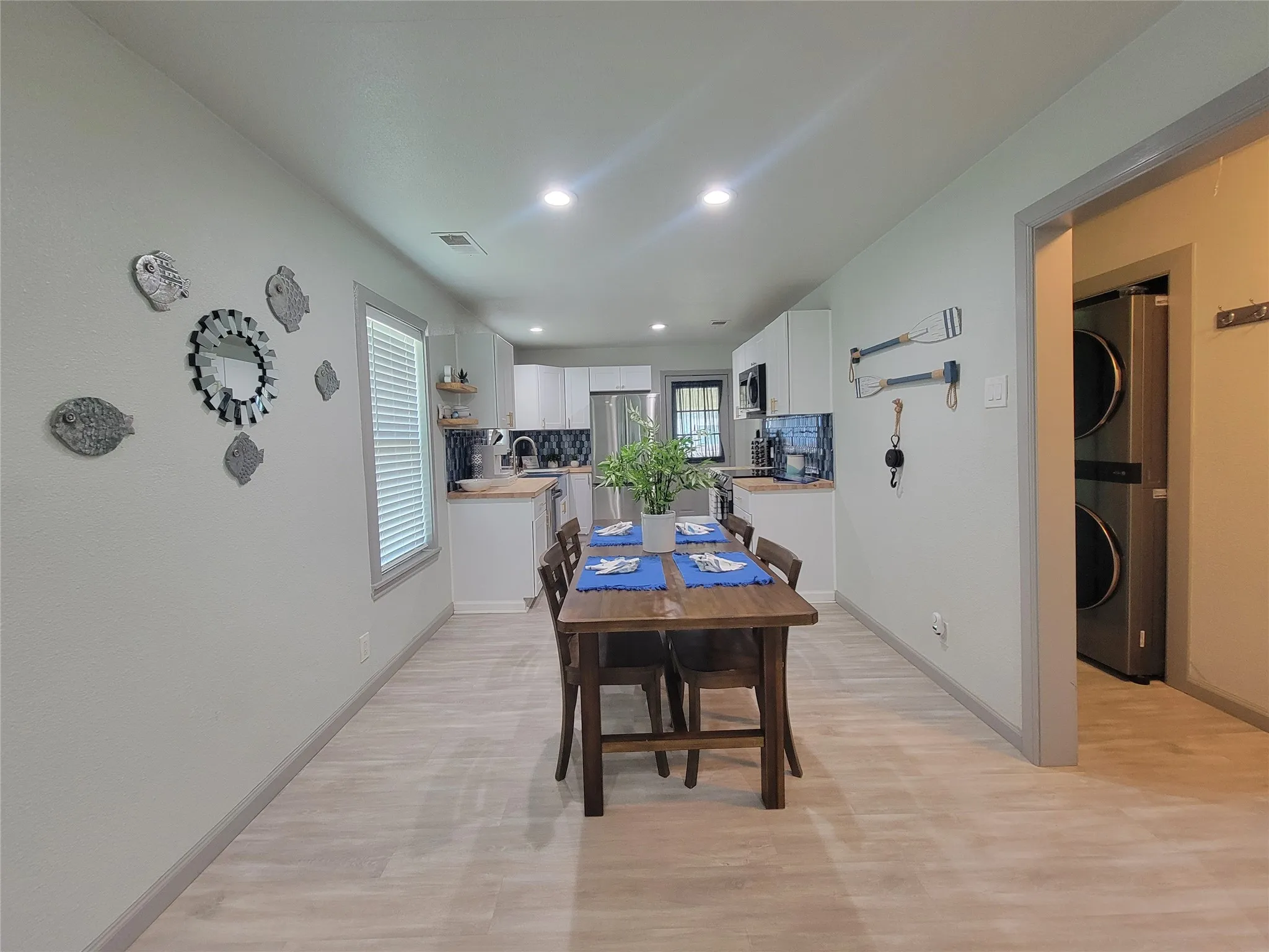 Open concept kitchen and dining area featuring light wood-finish flooring, recessed lighting, white cabinetry, and a dark tile backsplash