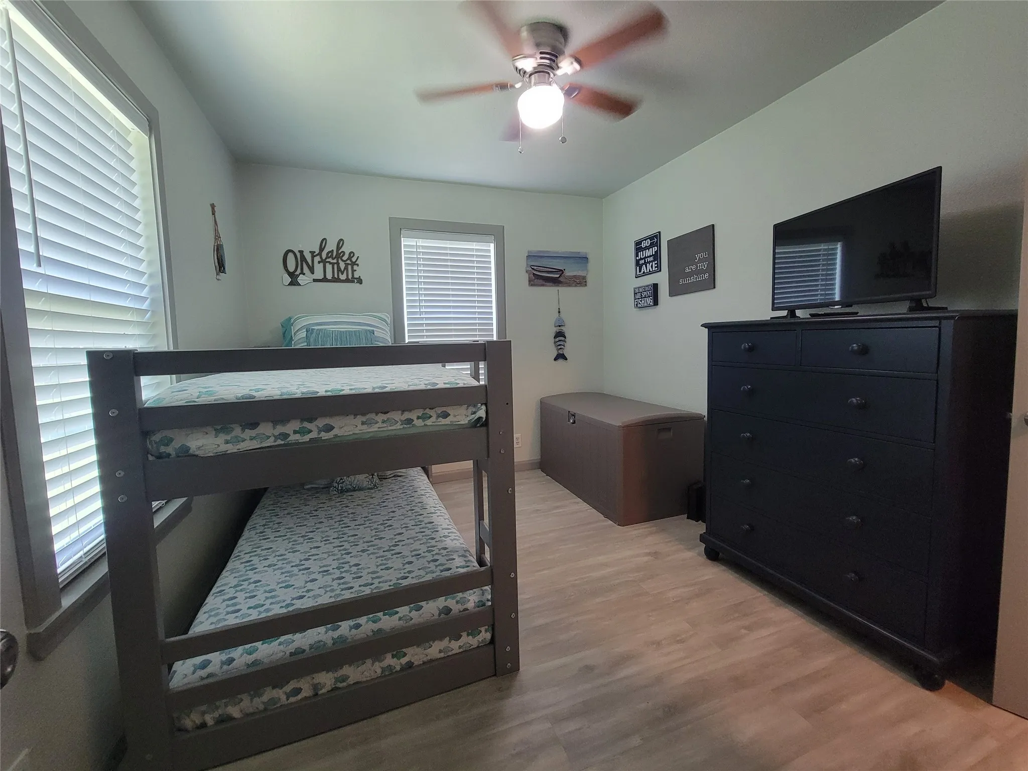 Room featuring a bunk bed, light-toned wood-finish flooring, and a ceiling fan with light fixture