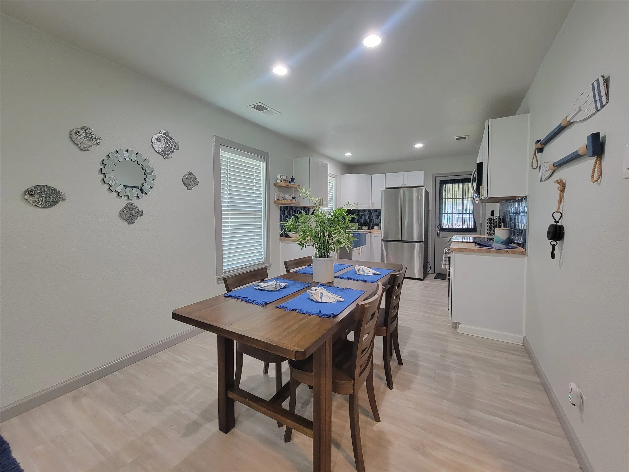 Open-concept living space featuring light wood-finish flooring, recessed lighting, white cabinetry, and a stainless steel refrigerator