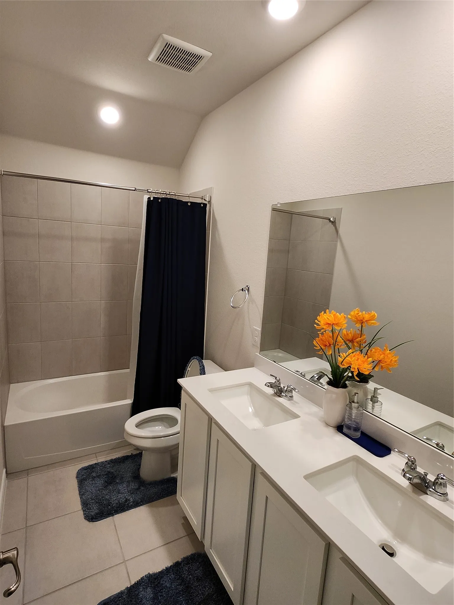 Bathroom featuring a dual vanity with white cabinetry and integrated sinks, a full-width mirror, and a bathtub with tile surround