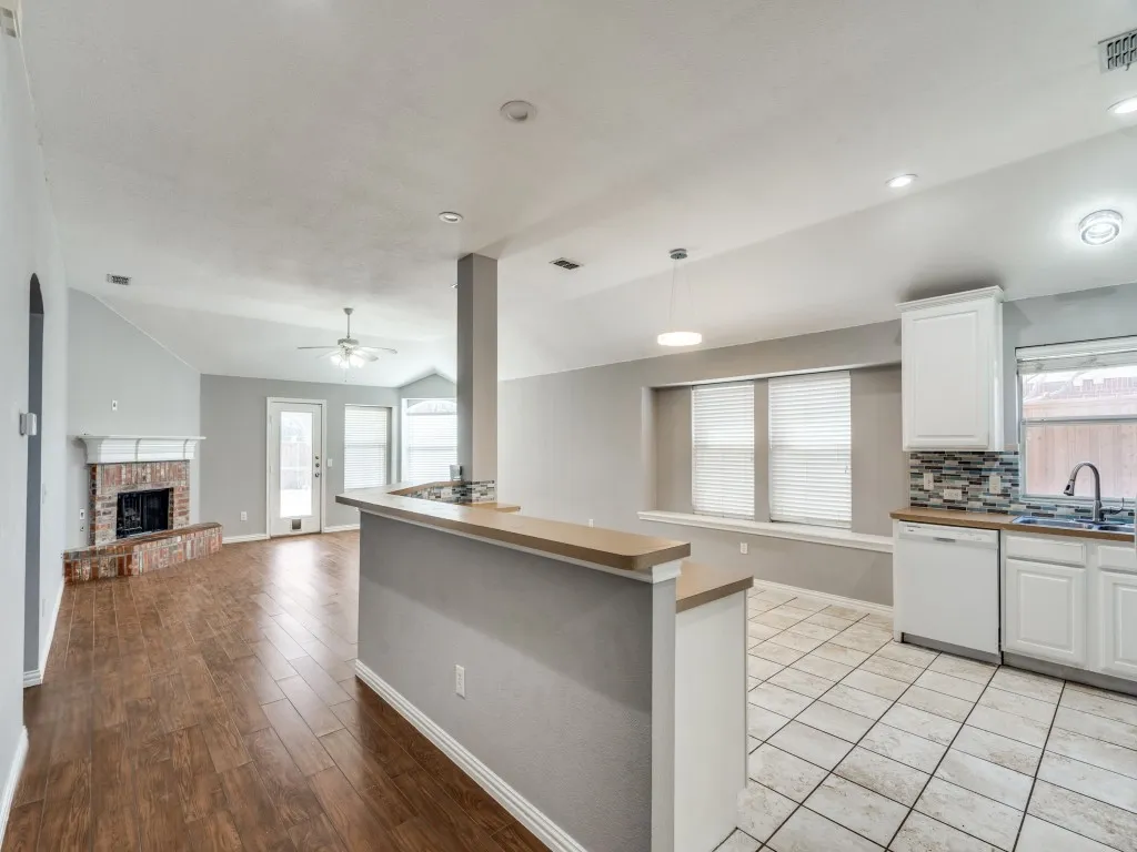 Kitchen with lofted ceiling, a brick fireplace, white dishwasher, and a sink