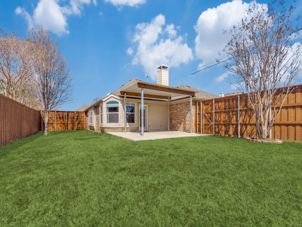Rear view of property with brick siding, a chimney, a fenced backyard, and a lawn