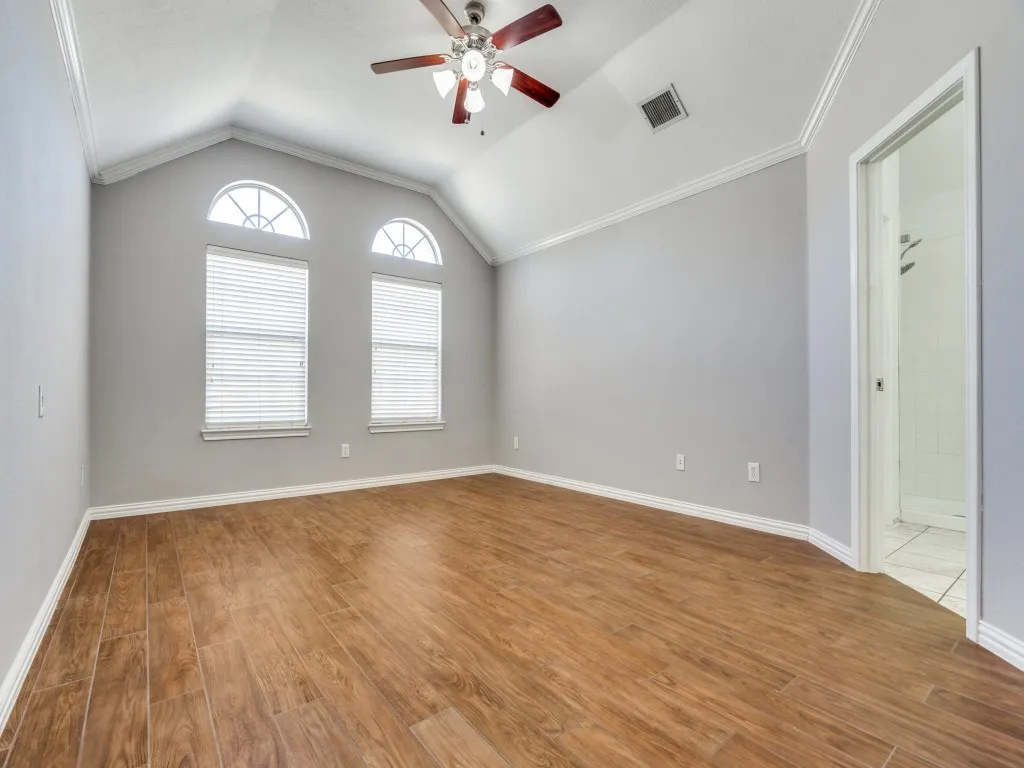 Unfurnished room featuring ceiling fan, visible vents, wood finished floors, and vaulted ceiling