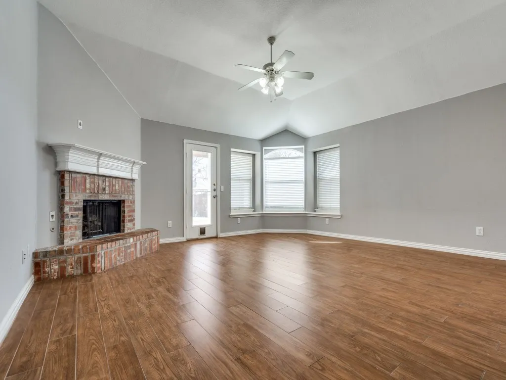 Unfurnished living room featuring a brick fireplace, baseboards, ceiling fan, vaulted ceiling, and wood finished floors