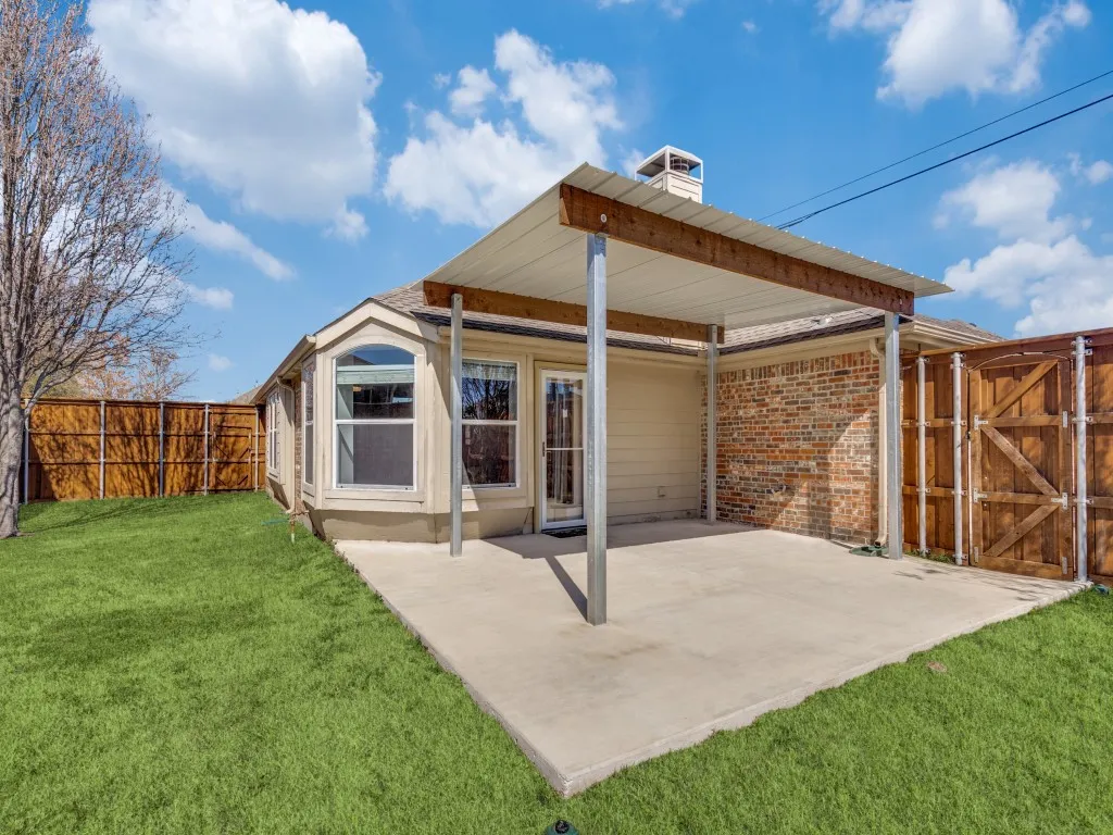 Back of house featuring a gate, fence, a yard, a patio area, and brick siding