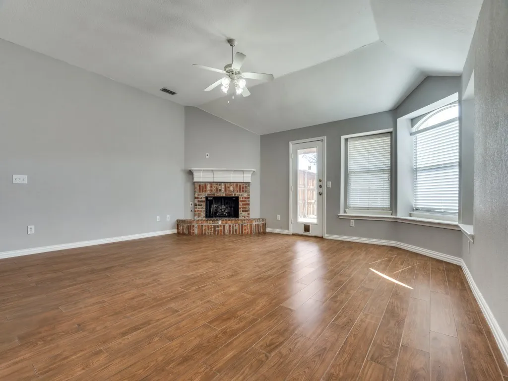 Unfurnished living room featuring visible vents, a brick fireplace, ceiling fan, lofted ceiling, and wood finished floors