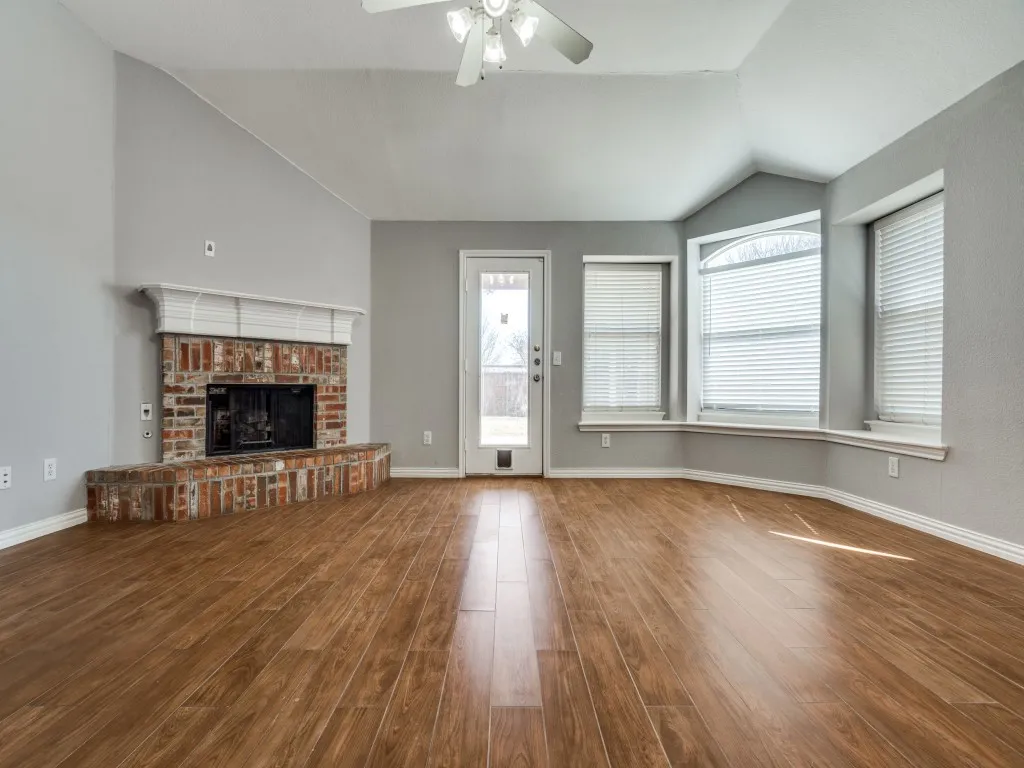 Unfurnished living room featuring lofted ceiling, a brick fireplace, wood finished floors, and a ceiling fan