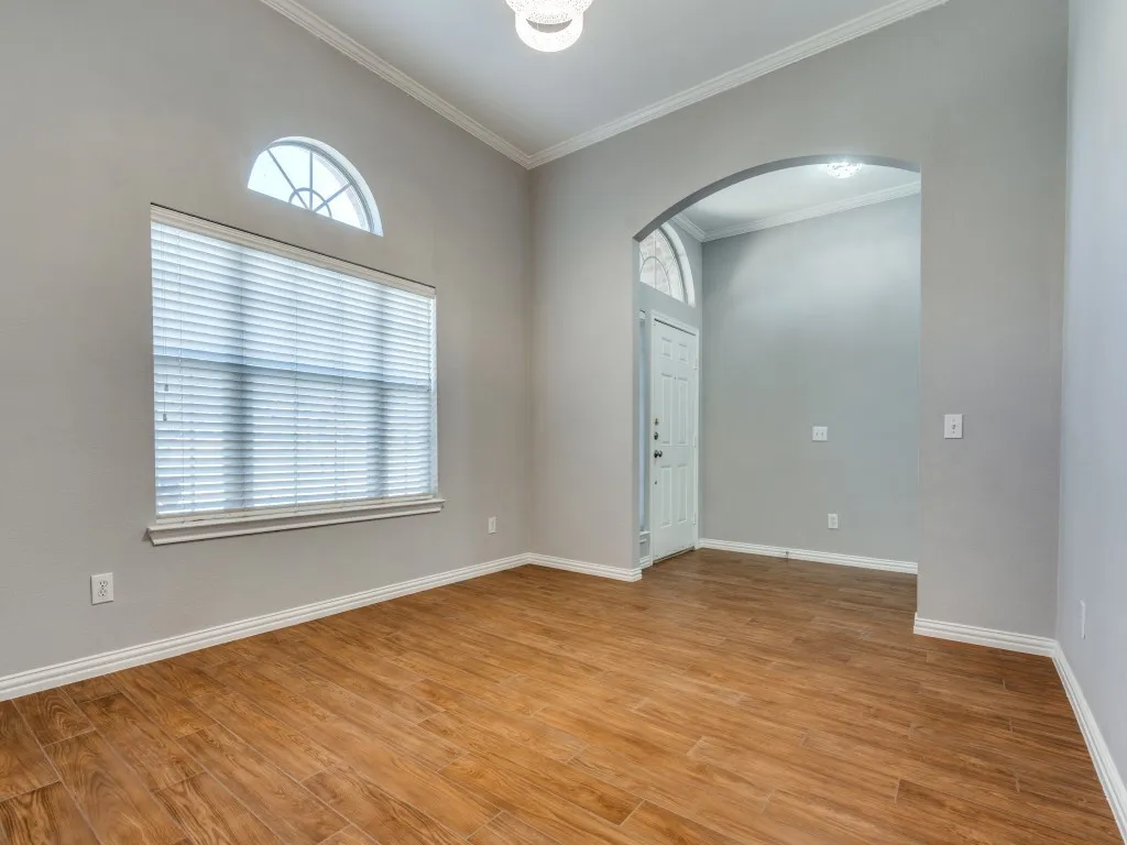 Empty room featuring arched walkways, light wood-style flooring, baseboards, and ornamental molding