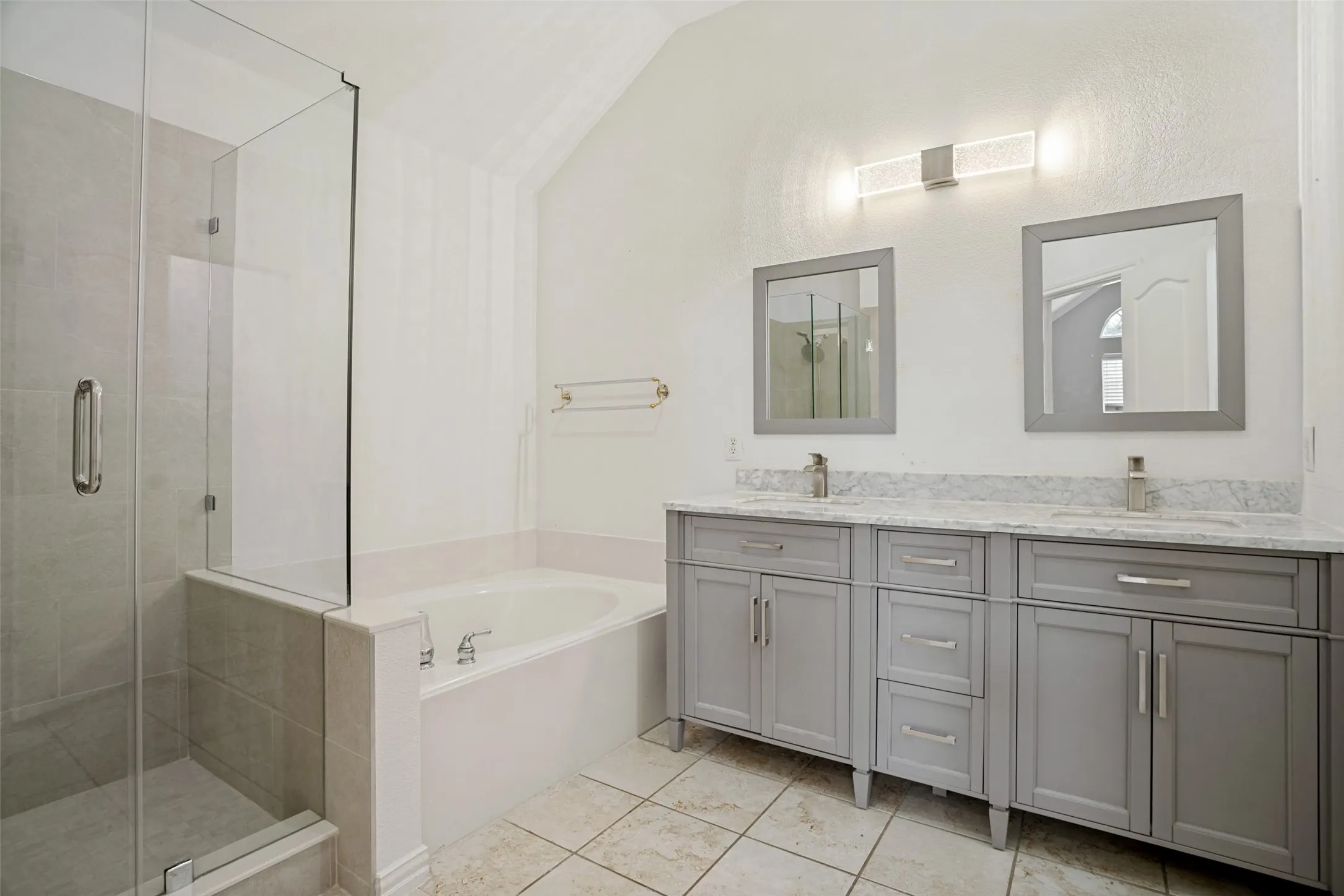Spacious bathroom featuring a glass-enclosed shower, built-in soaking tub, a dual vanity with light gray cabinetry, and stone-finish countertops