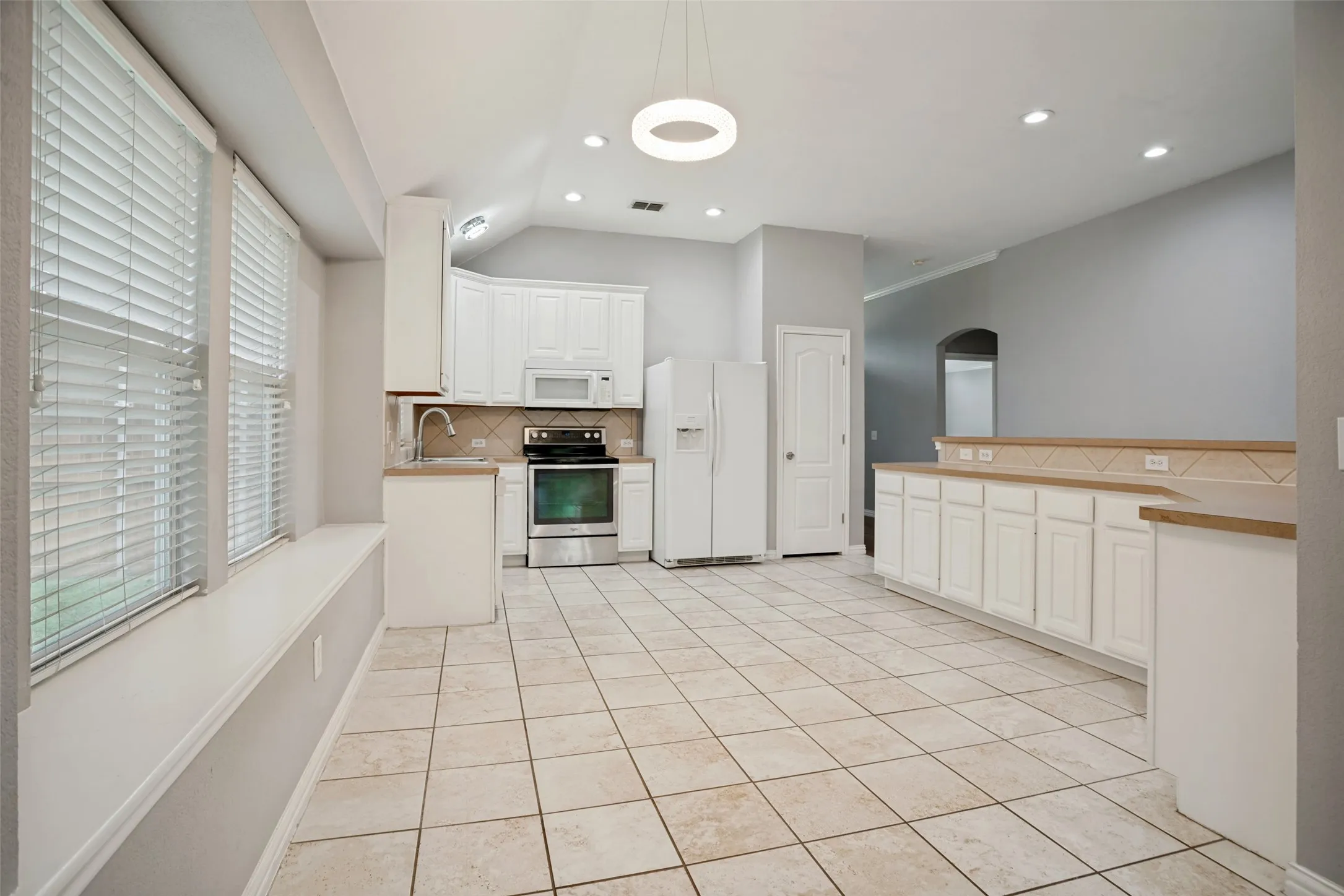 Spacious kitchen featuring white cabinetry, tile flooring, recessed lighting, and a contemporary circular pendant light fixture