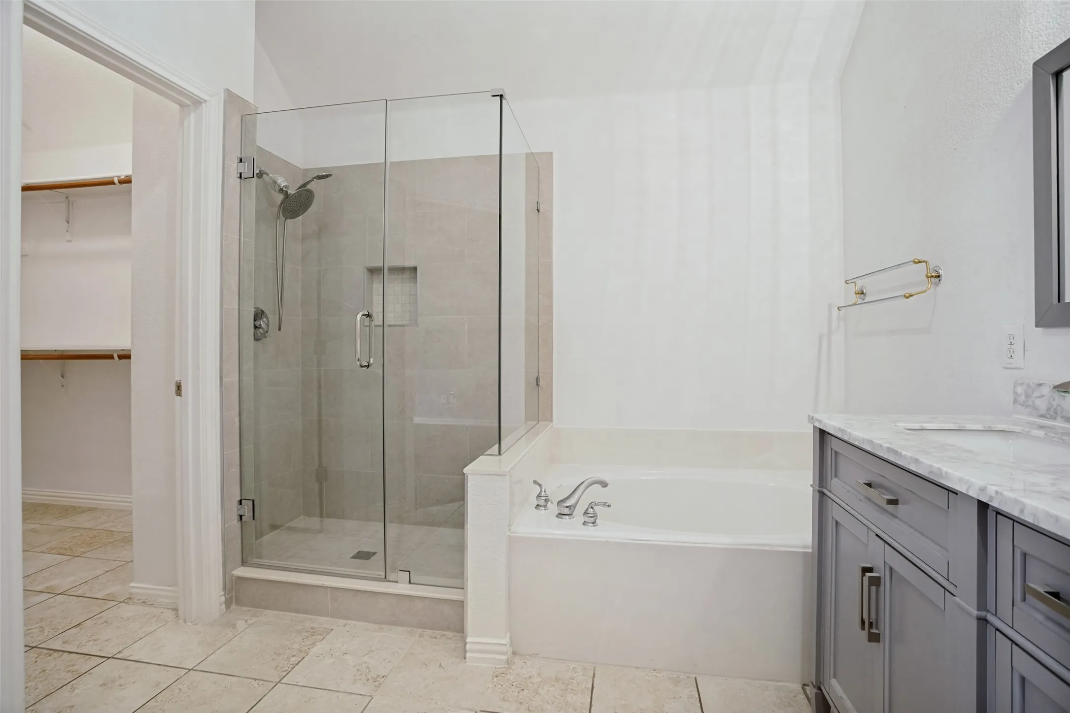 Bathroom featuring a glass-enclosed shower, built-in bathtub, dual-sink vanity with a stone countertop, and tile flooring